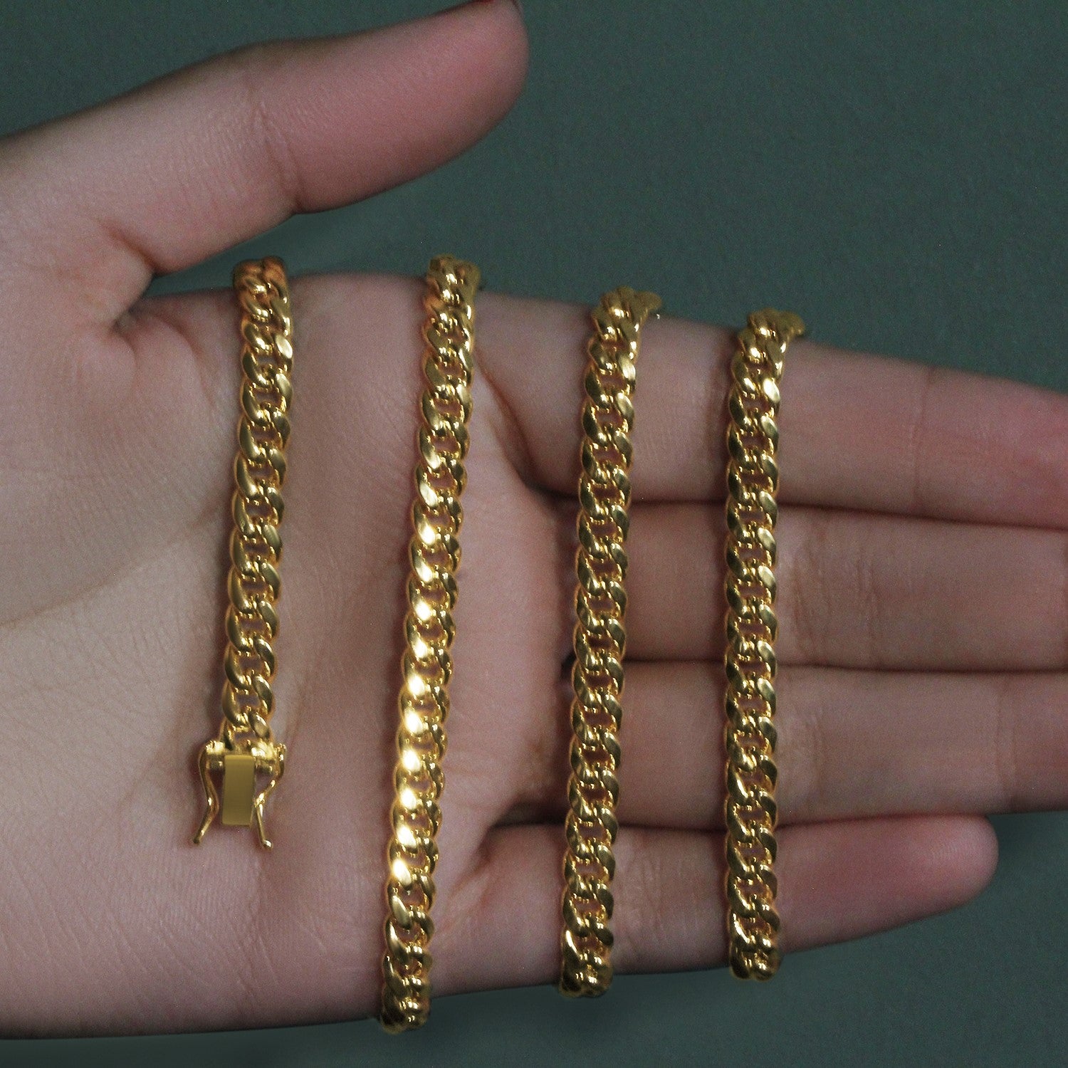 Four 14k yellow gold semi-solid Miami Cuban chains, 5mm wide, held in a hand.