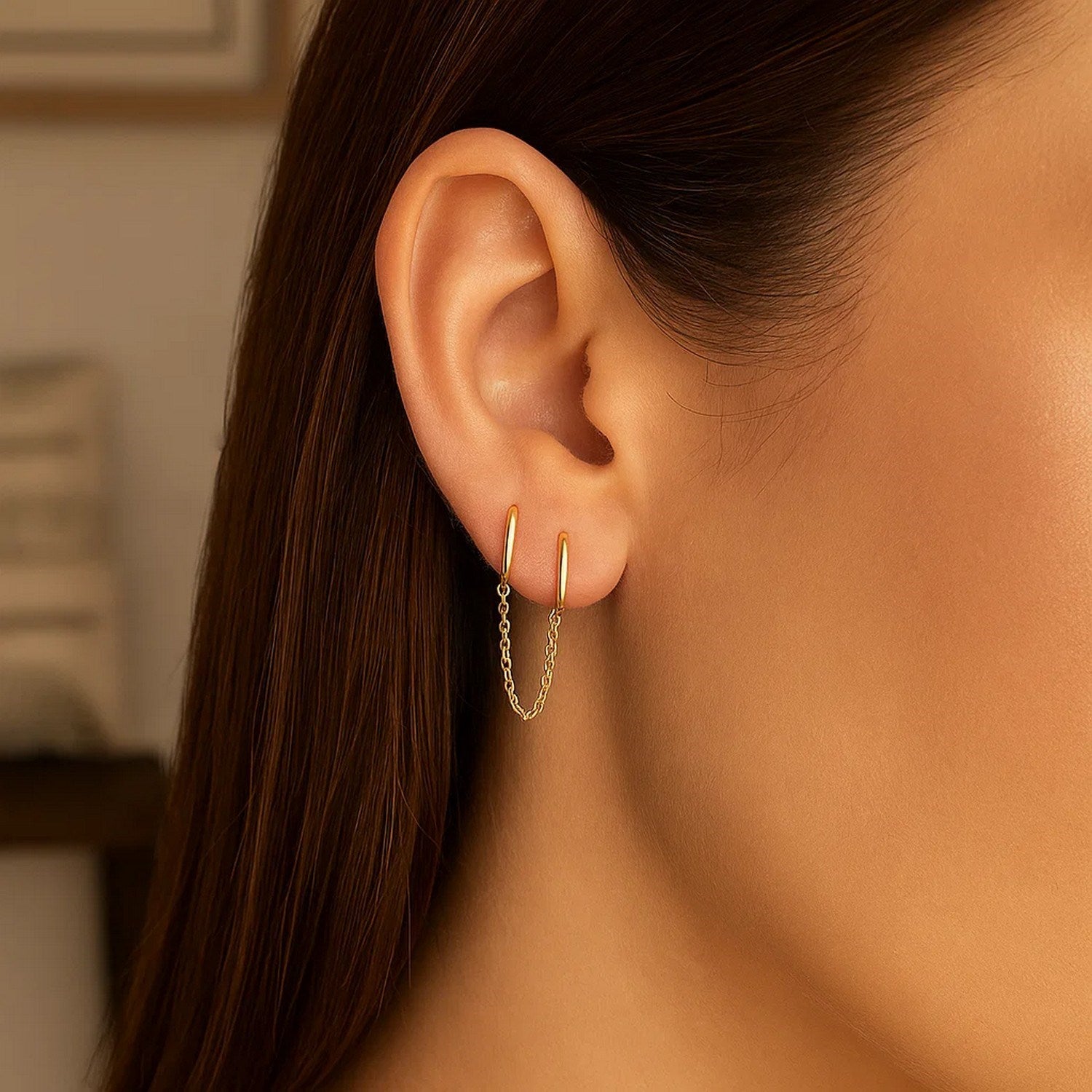 14k yellow gold two-hole huggie style hoop earrings with a delicate chain.