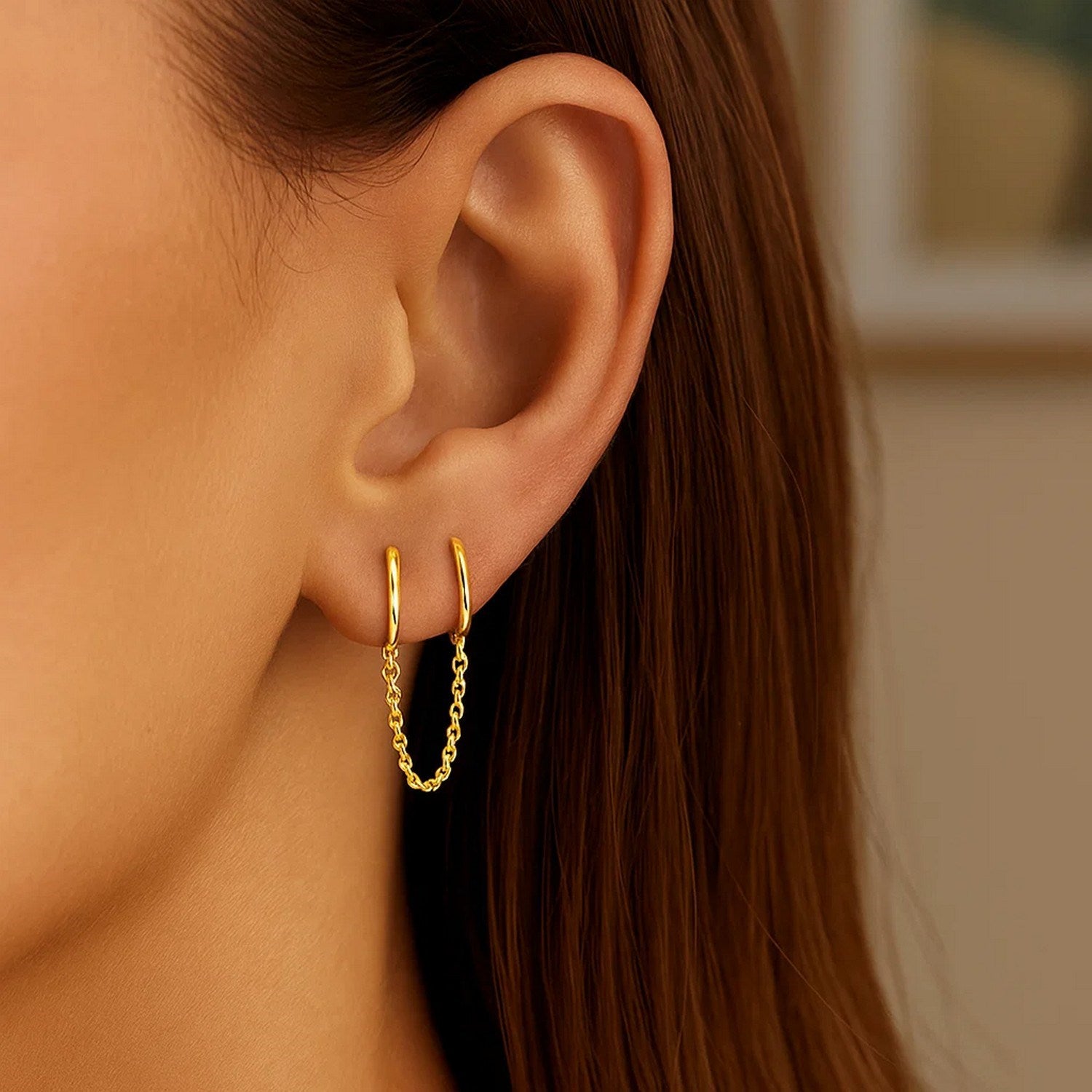 14k yellow gold two-hole huggie style hoop earrings with a delicate chain.