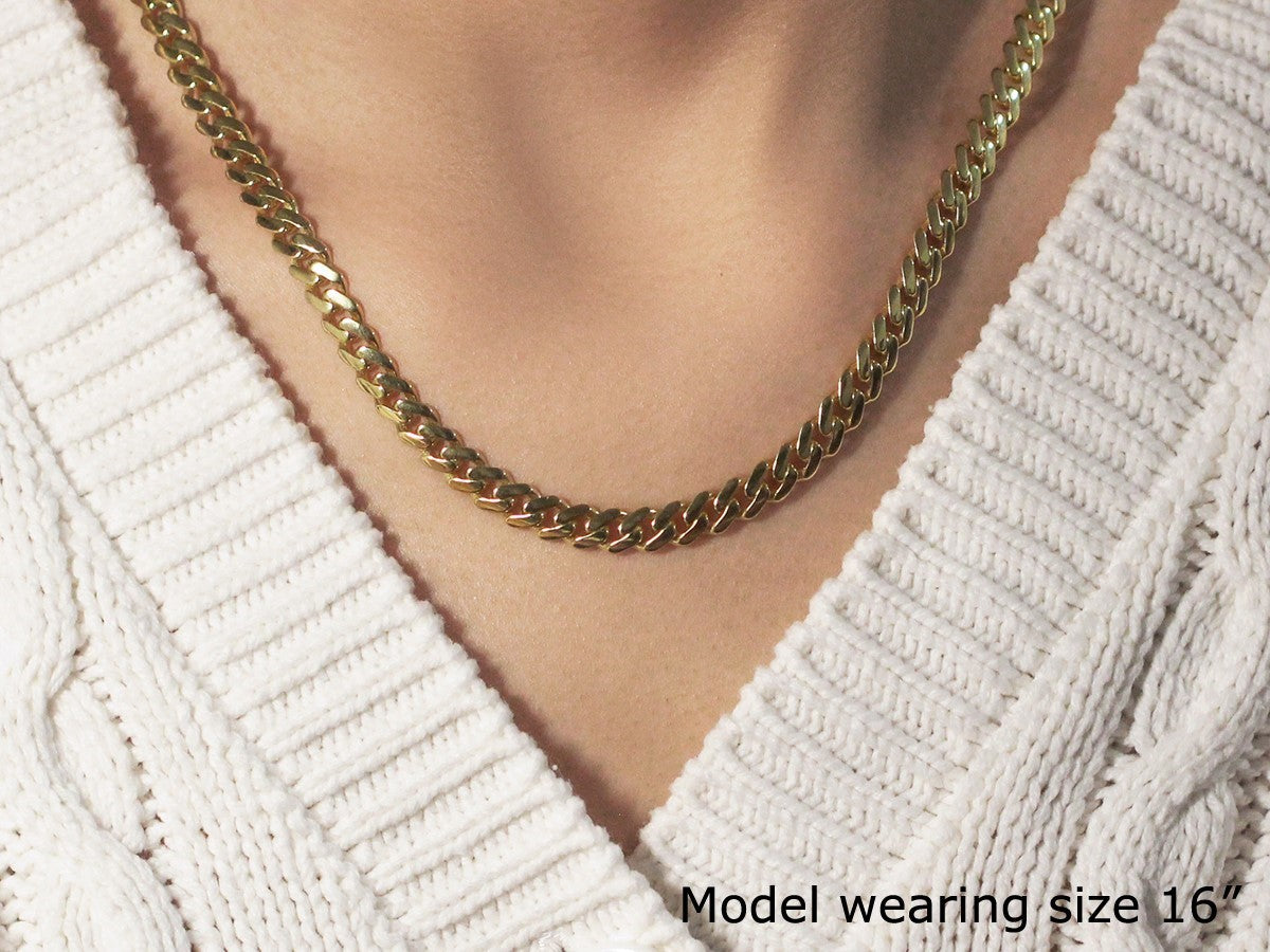 A polished 14k yellow gold Miami Cuban chain necklace on a model wearing a white sweater.