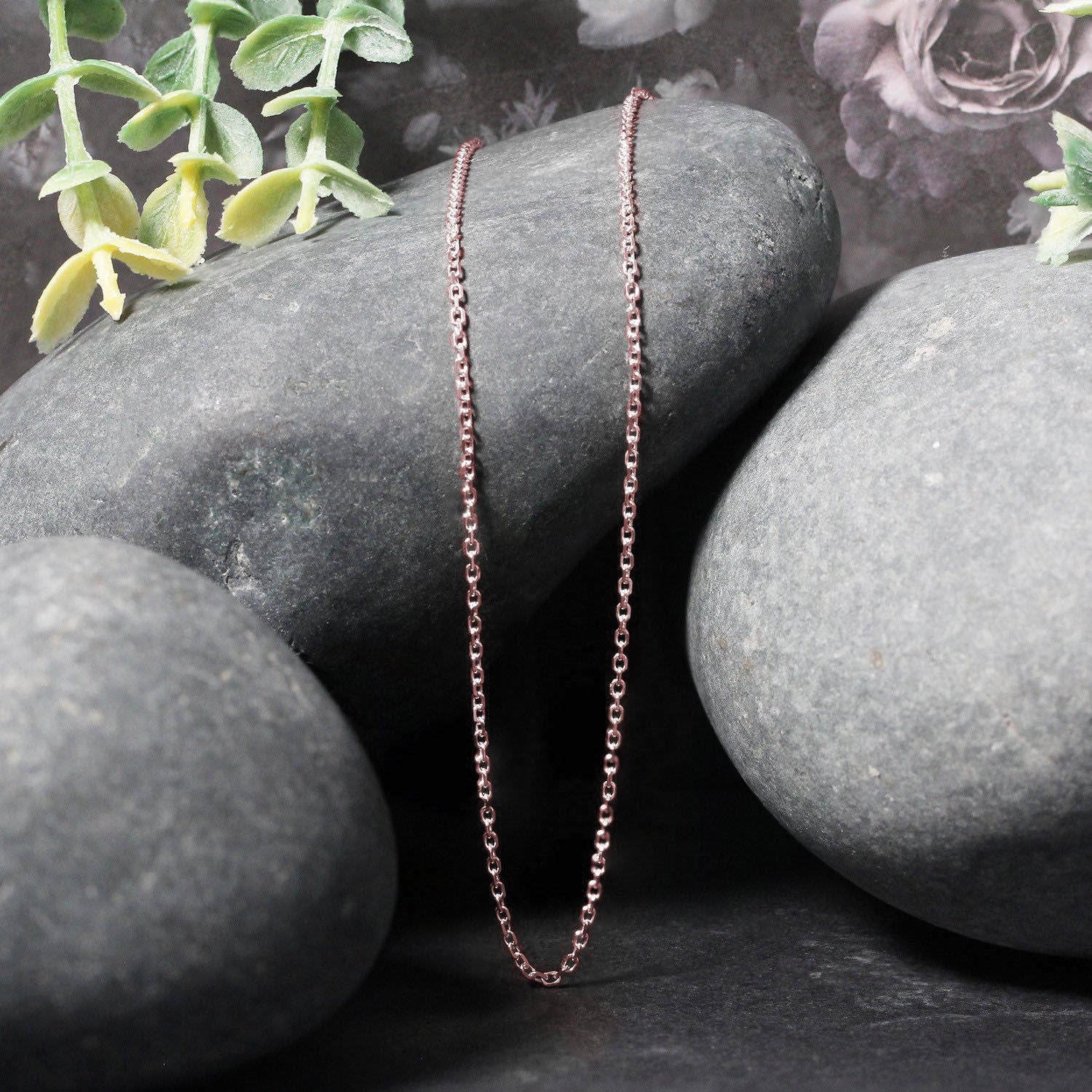 A 14k rose gold diamond cut cable link chain is draped over dark grey stones.