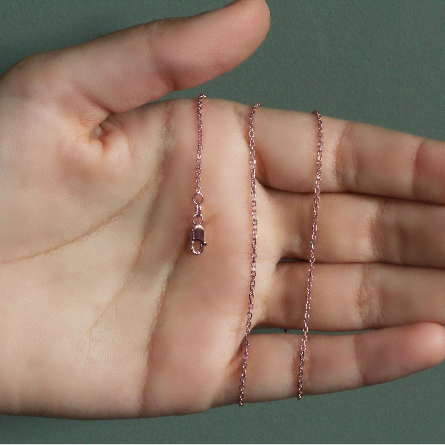 14k rose gold diamond cut cable link chain with a lobster clasp on a hand.