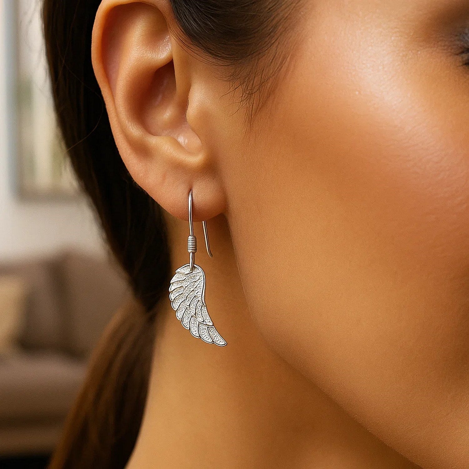 Sterling silver textured angel wing earrings hang from a woman's ear.