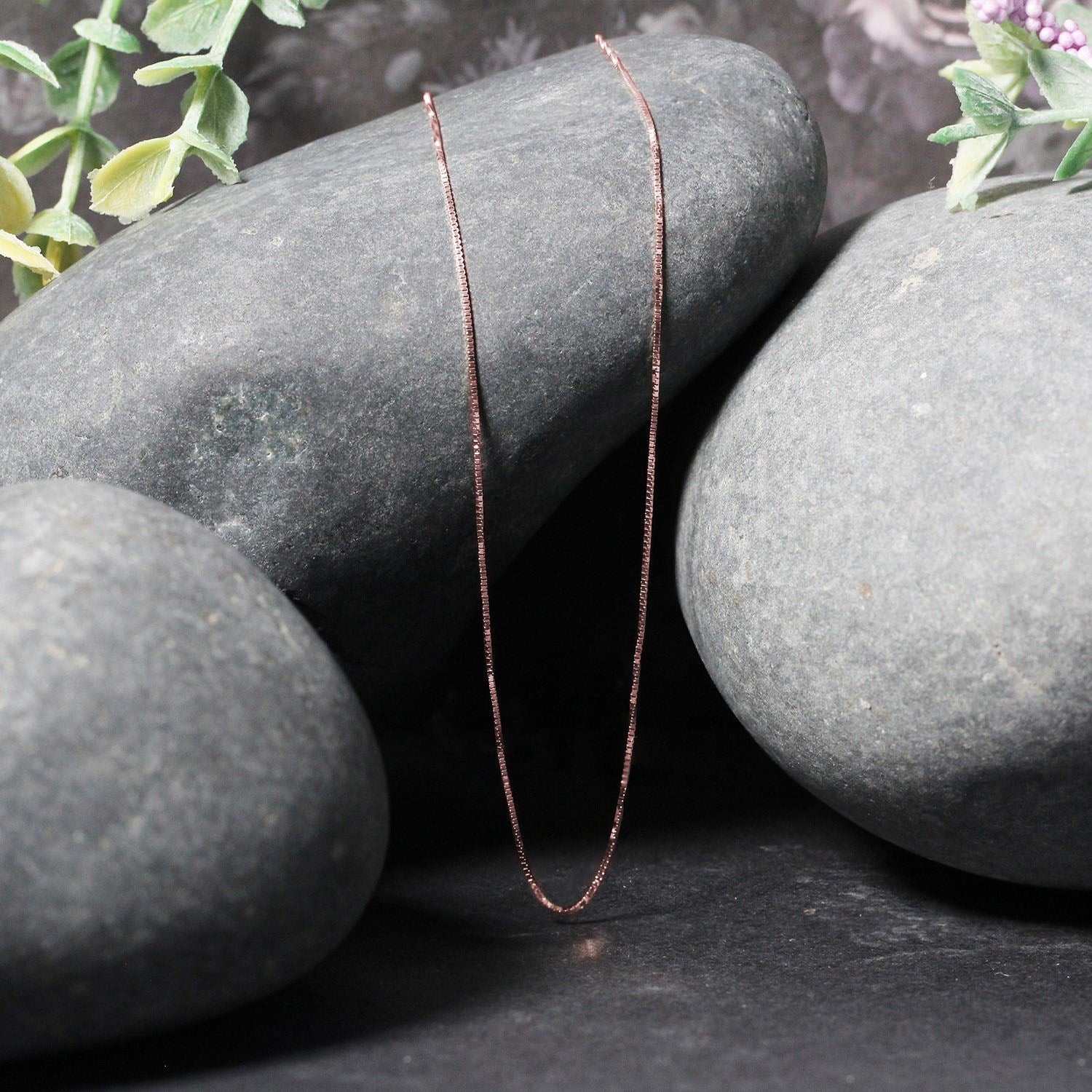 18k rose gold classic box chain draped over smooth gray stones.