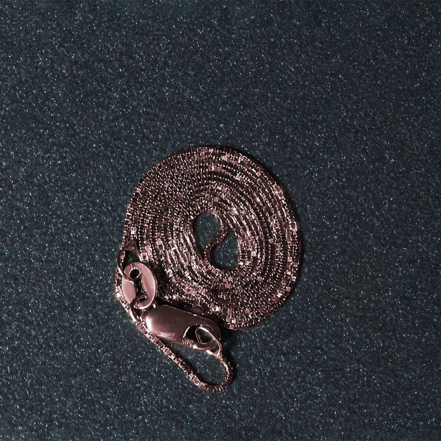18k rose gold classic box chain with a lobster clasp, coiled on a dark, glittery surface.