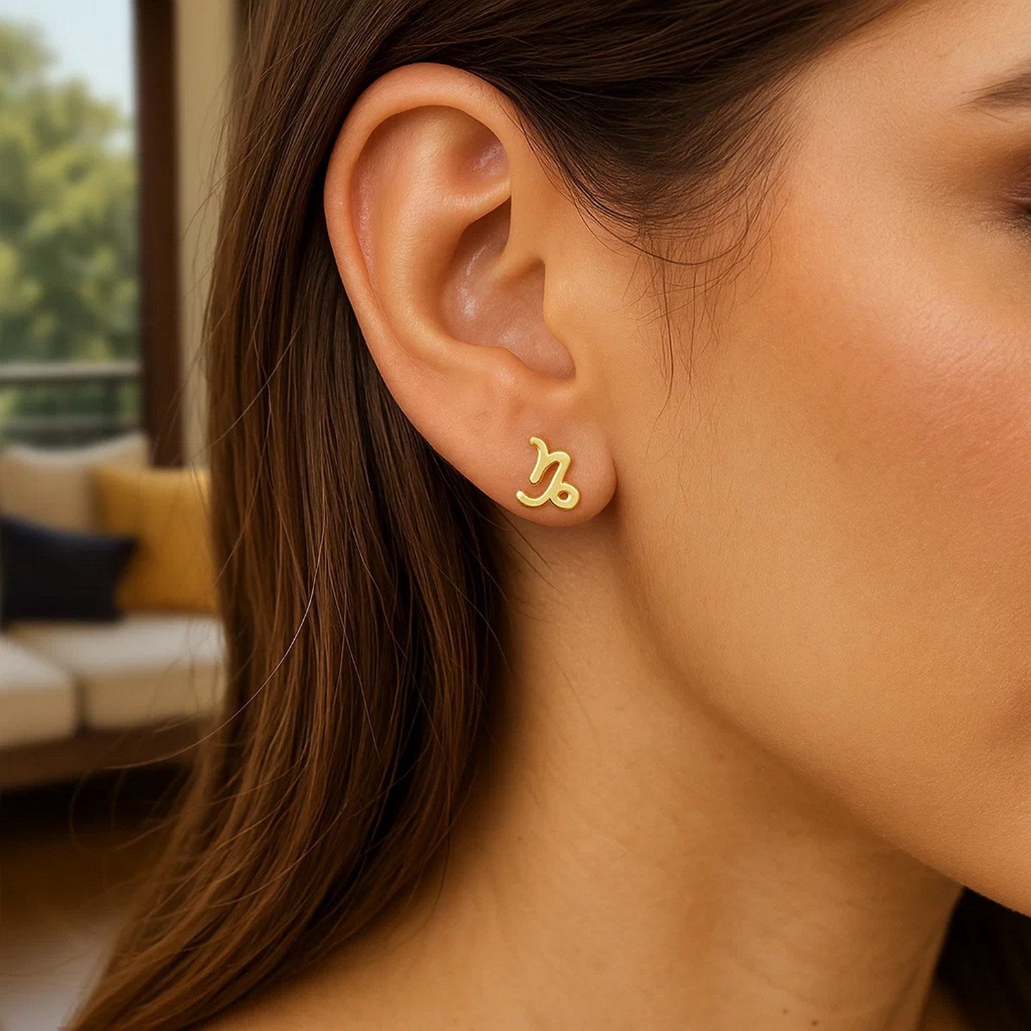 A close-up of a woman wearing a single 14k yellow gold Capricorn stud earring.