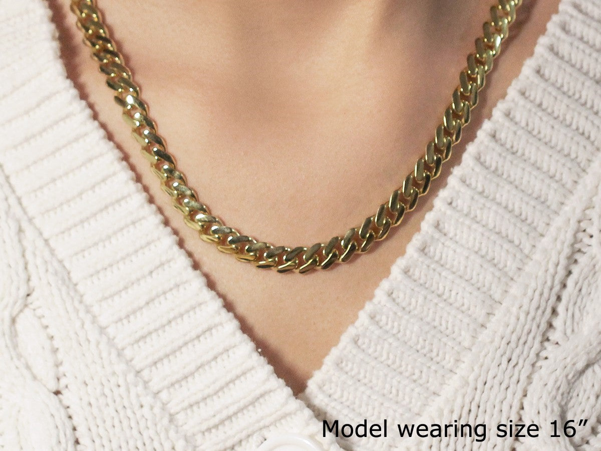 A polished 14k yellow gold Miami Cuban chain necklace on a model wearing a white sweater.
