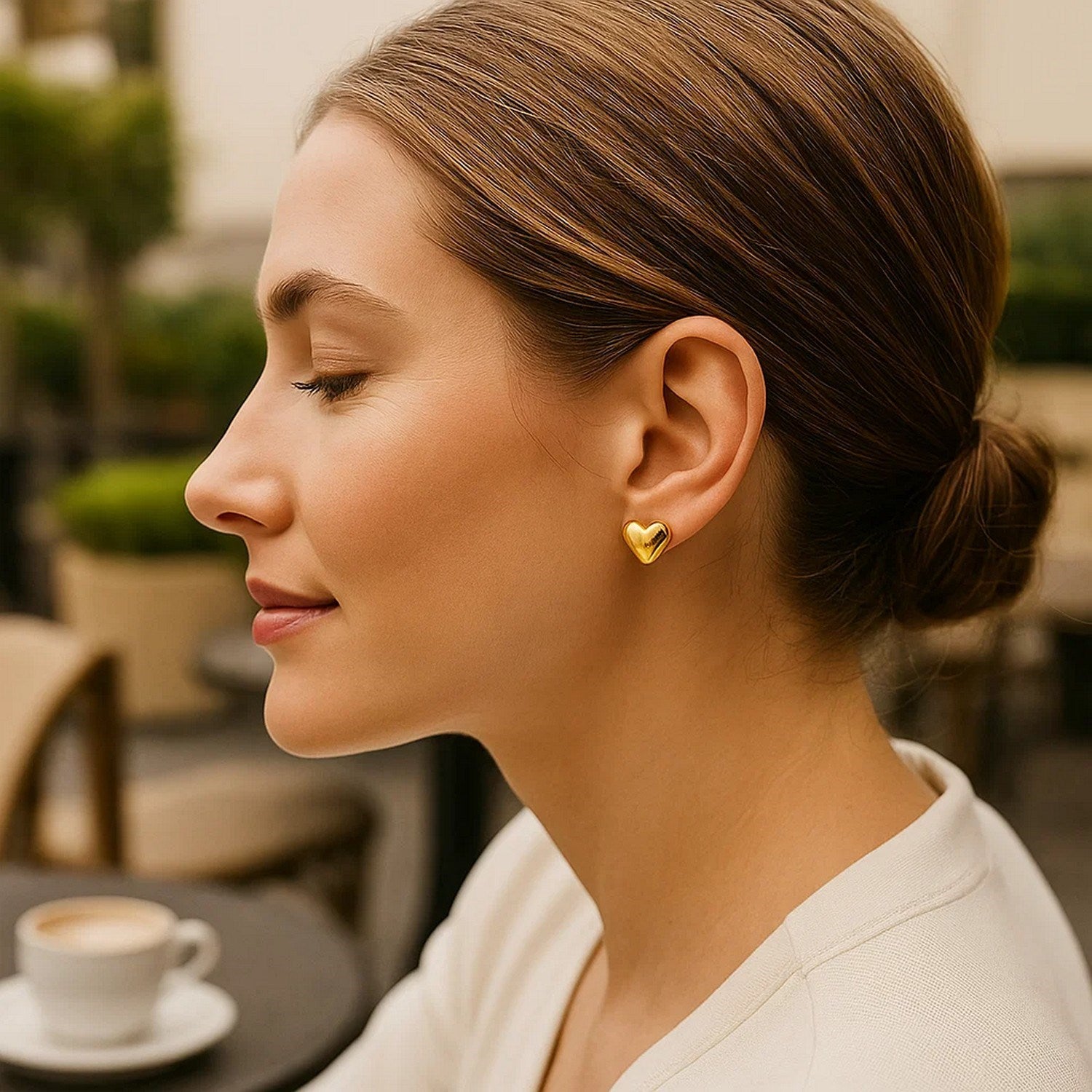 Puffed heart stud earrings in 14K yellow gold on a woman's ear.