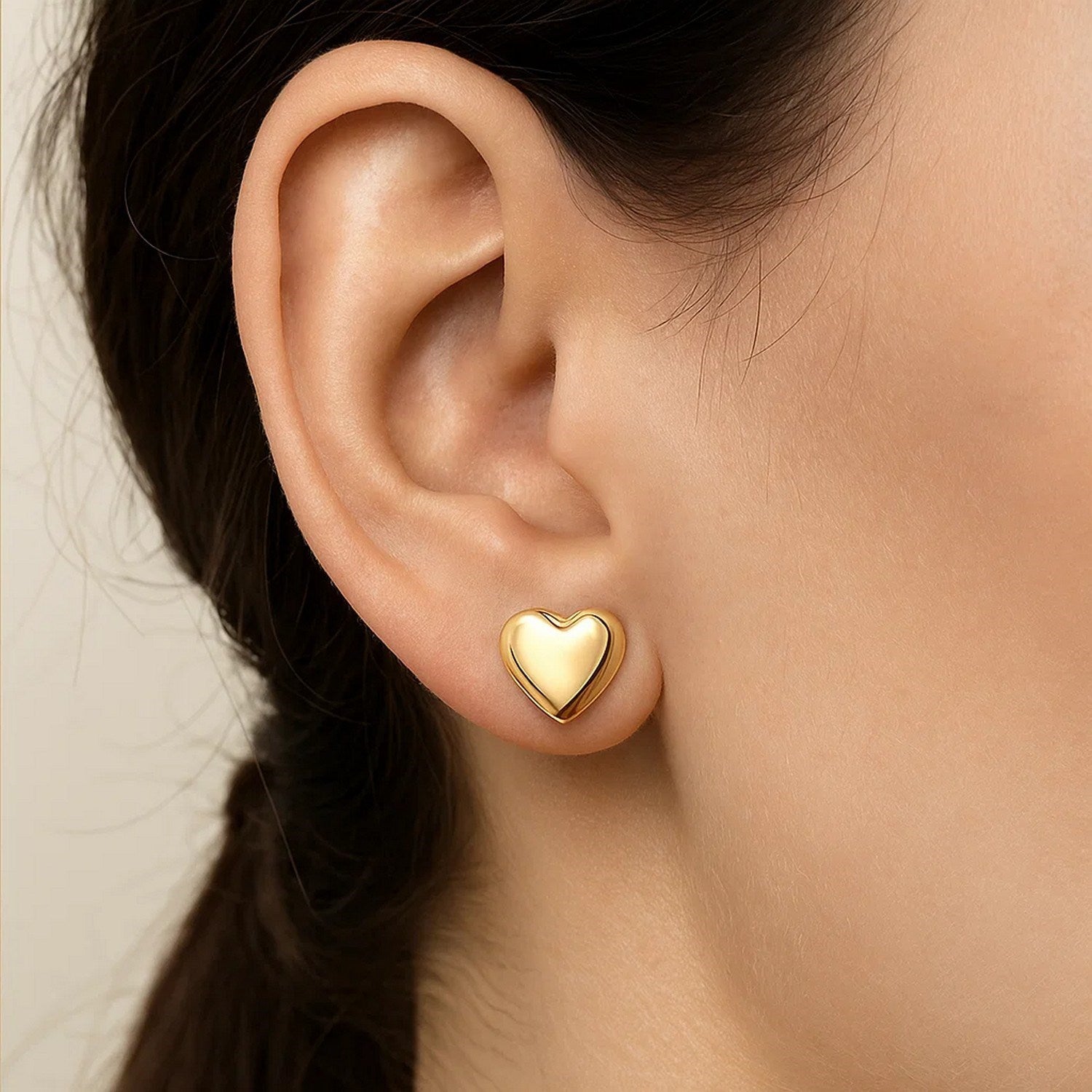 A woman wears a single puffed heart stud earring in 14K yellow gold.