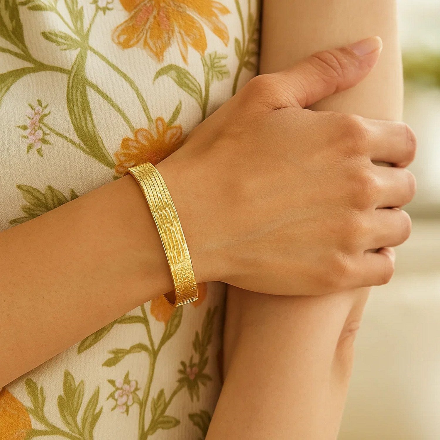 A woman wears a textured 14K yellow gold bracelet on her left wrist.
