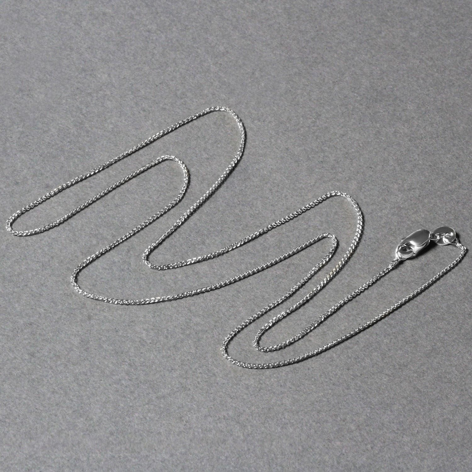 14k white gold round wheat chain with a lobster clasp on a gray background.