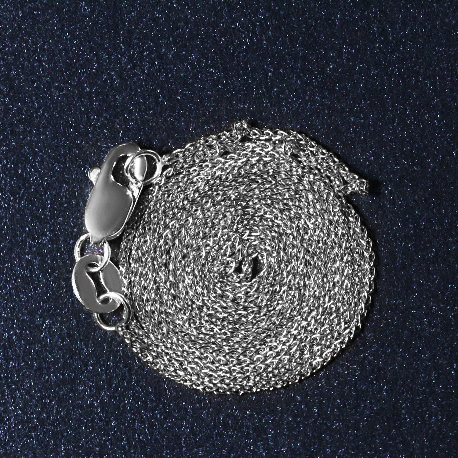 A coiled 14k white gold round wheat chain with a lobster clasp on a dark, glittery surface.