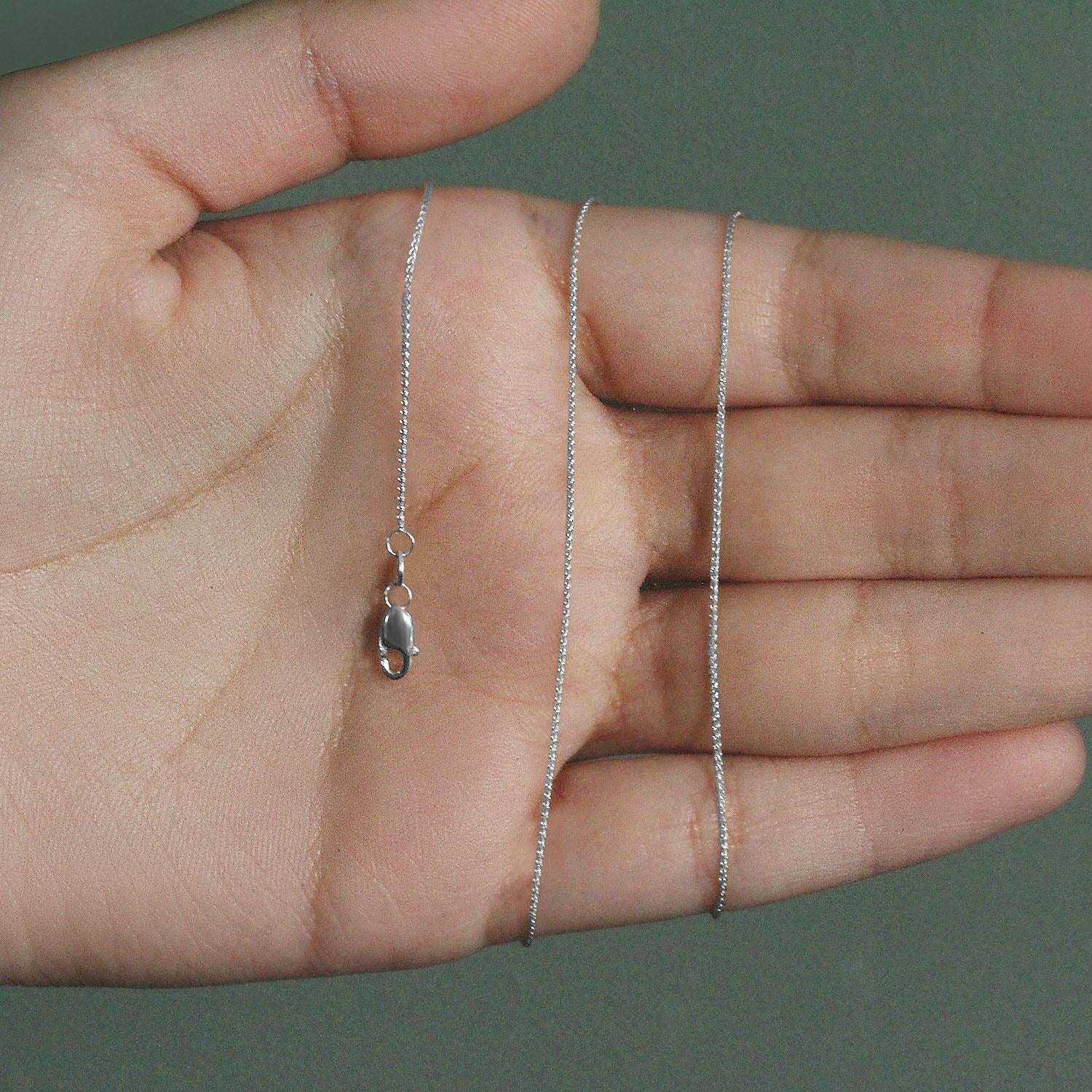 A 14k white gold round wheat chain with a lobster clasp is held in a hand.