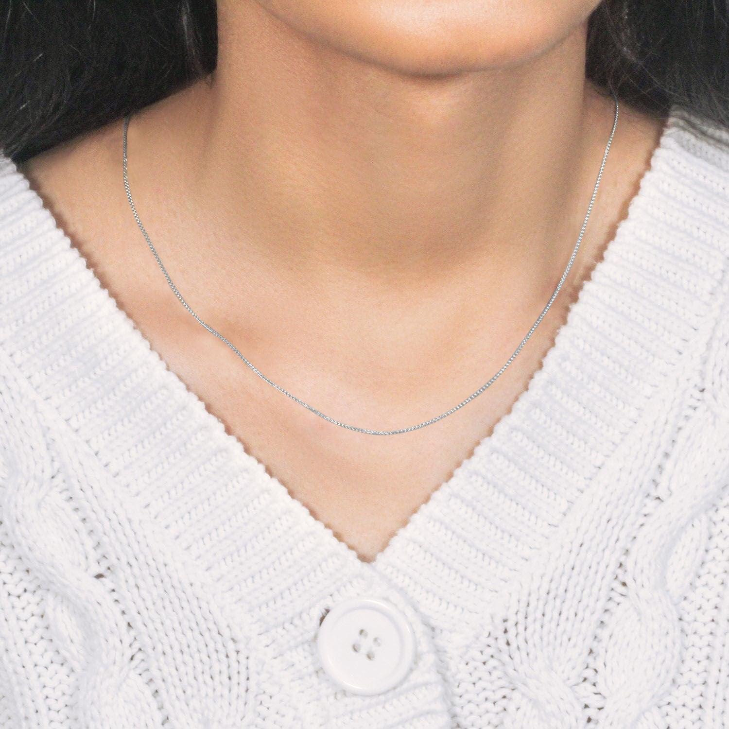 14k white gold round wheat chain on a person wearing a white cable-knit sweater.