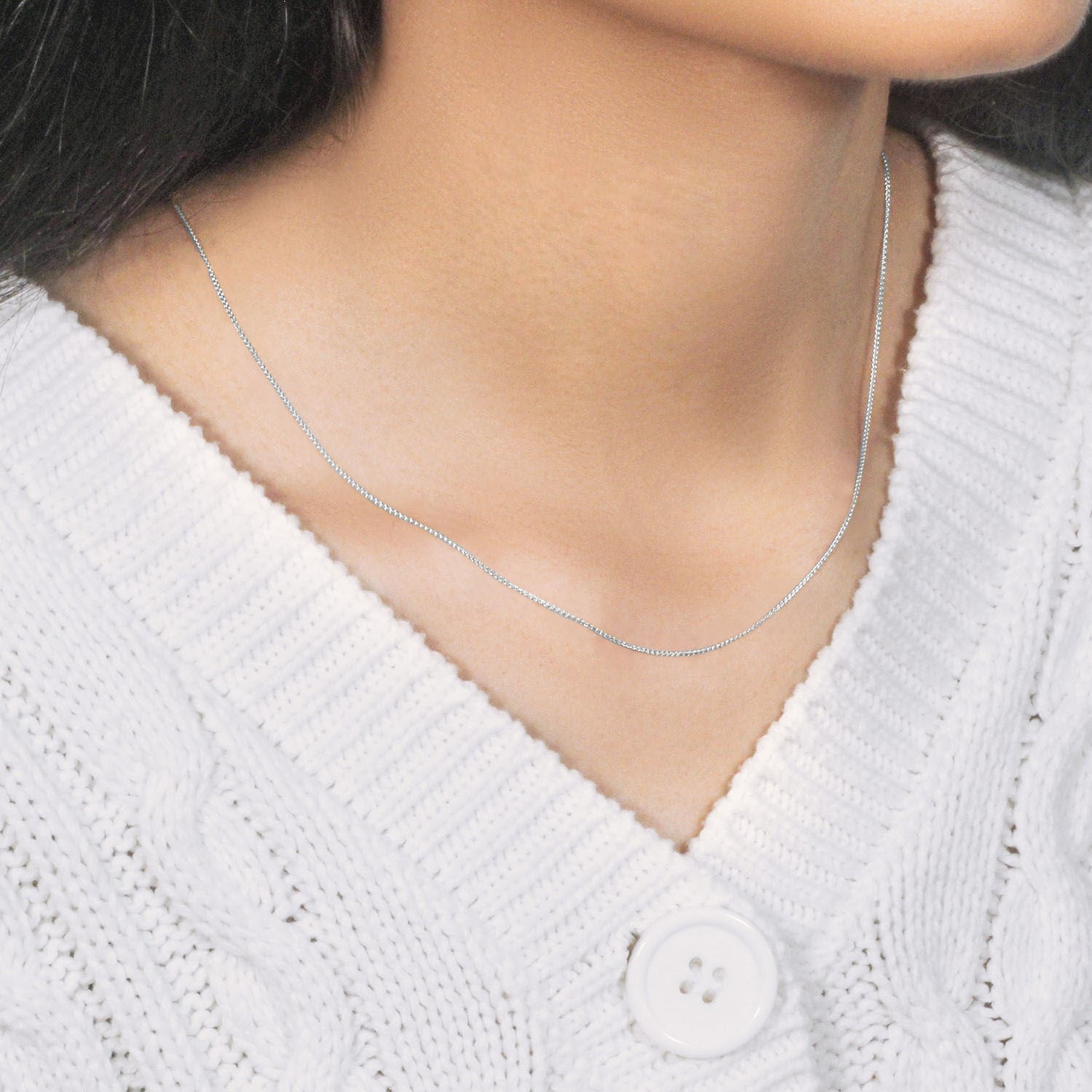 A 14k white gold round wheat chain is worn around a person's neck.