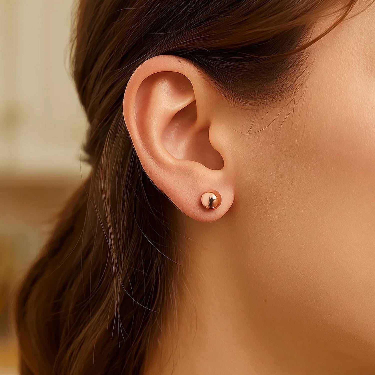 14k rose gold classic round shape stud earrings on a model's ear.