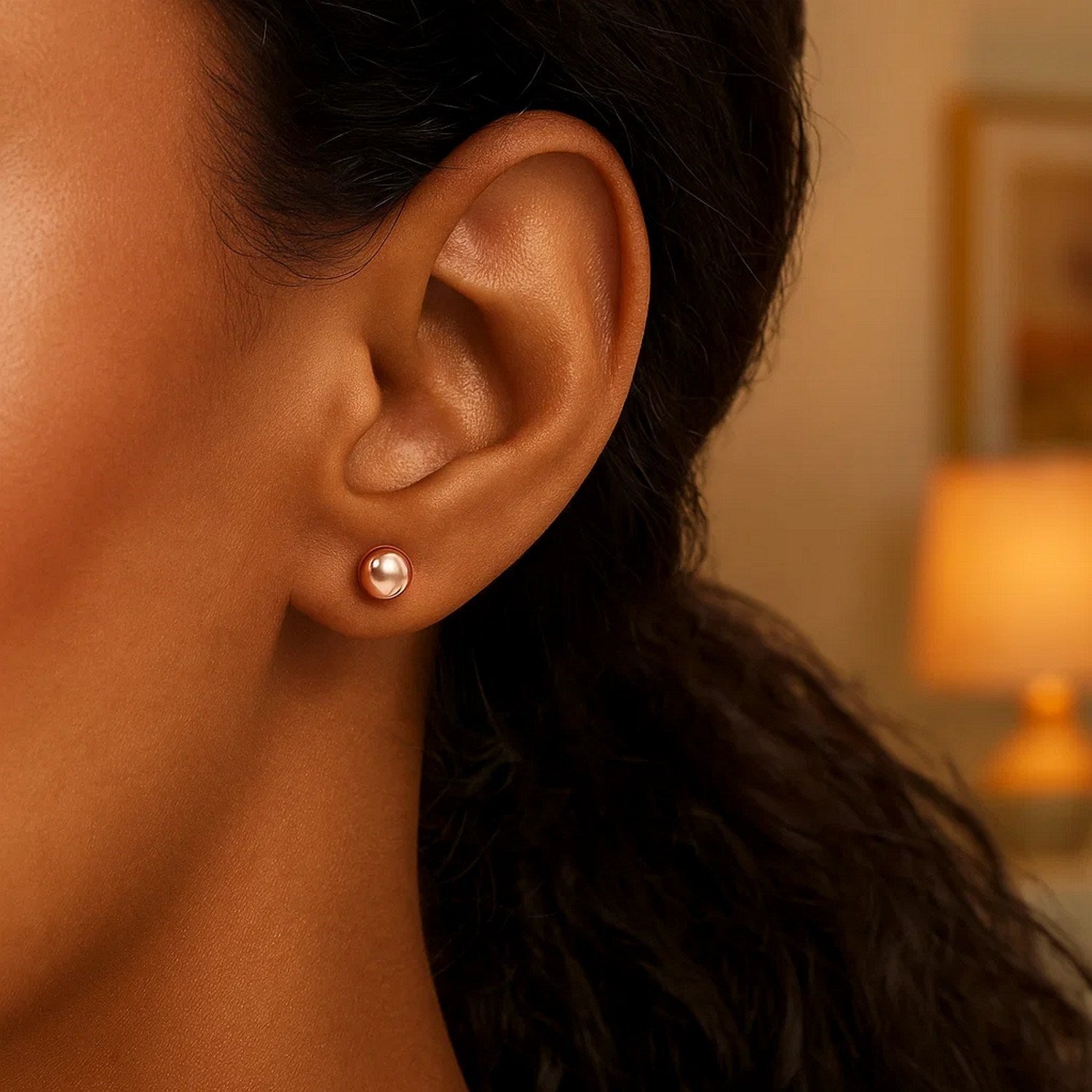 A single 6mm round rose gold stud earring is worn on an ear.