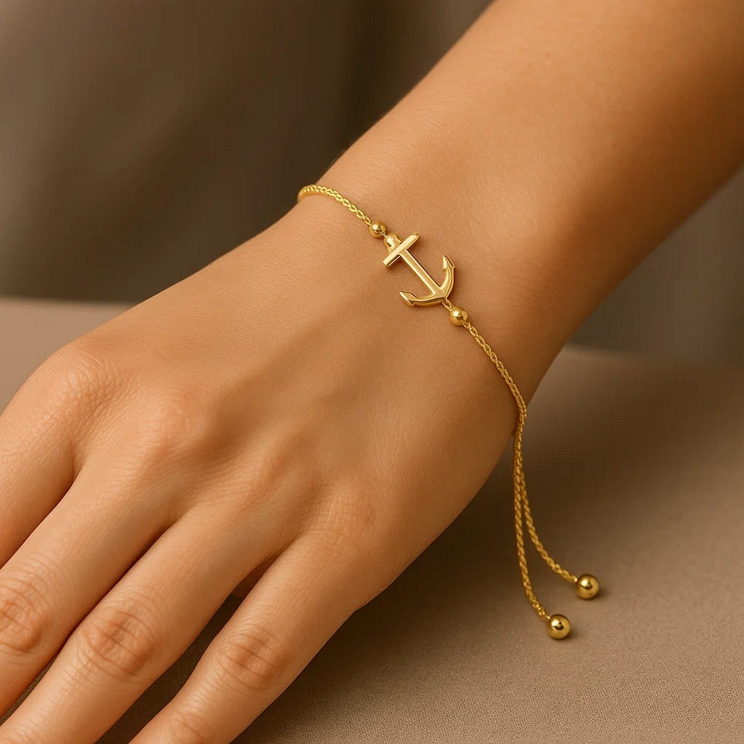 14k yellow gold anchor design adjustable lariat bracelet on a person's wrist.
