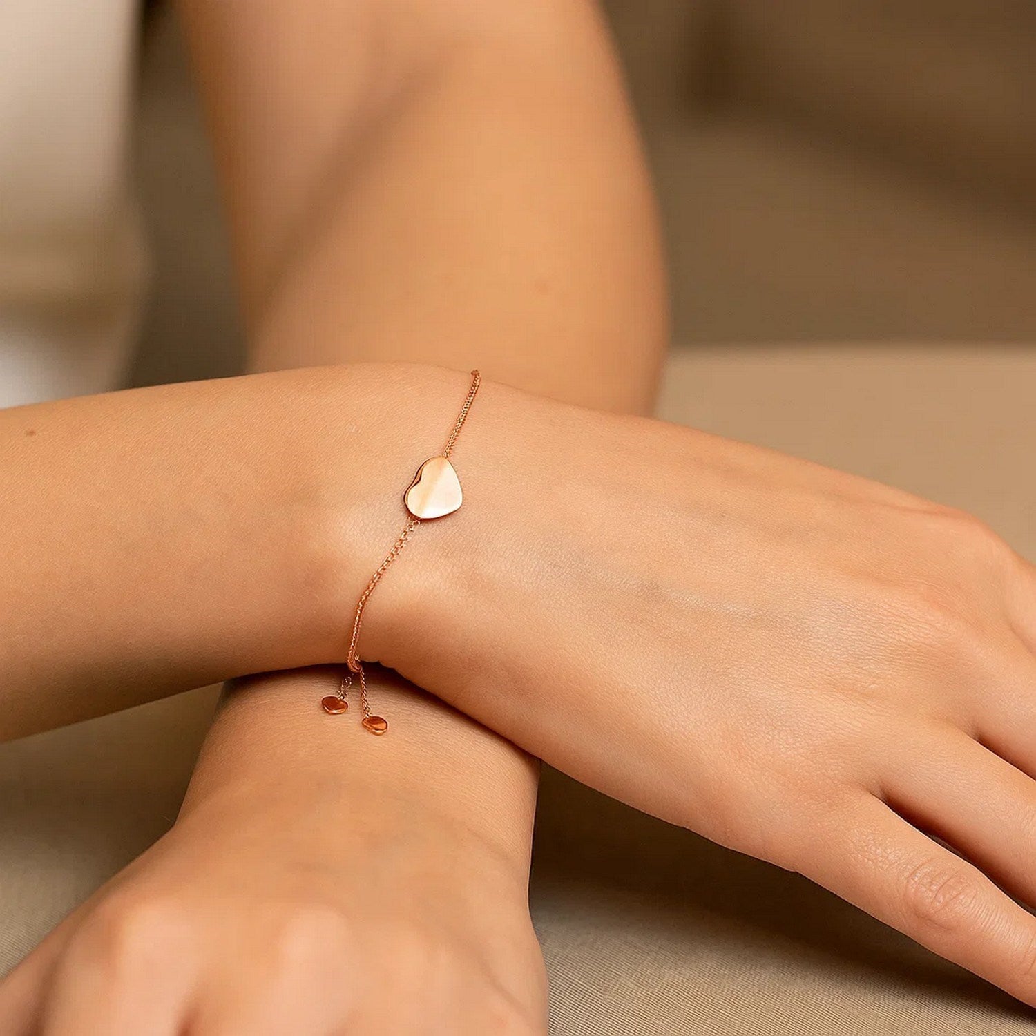A rose gold adjustable bracelet with a polished heart charm on a person's wrist.