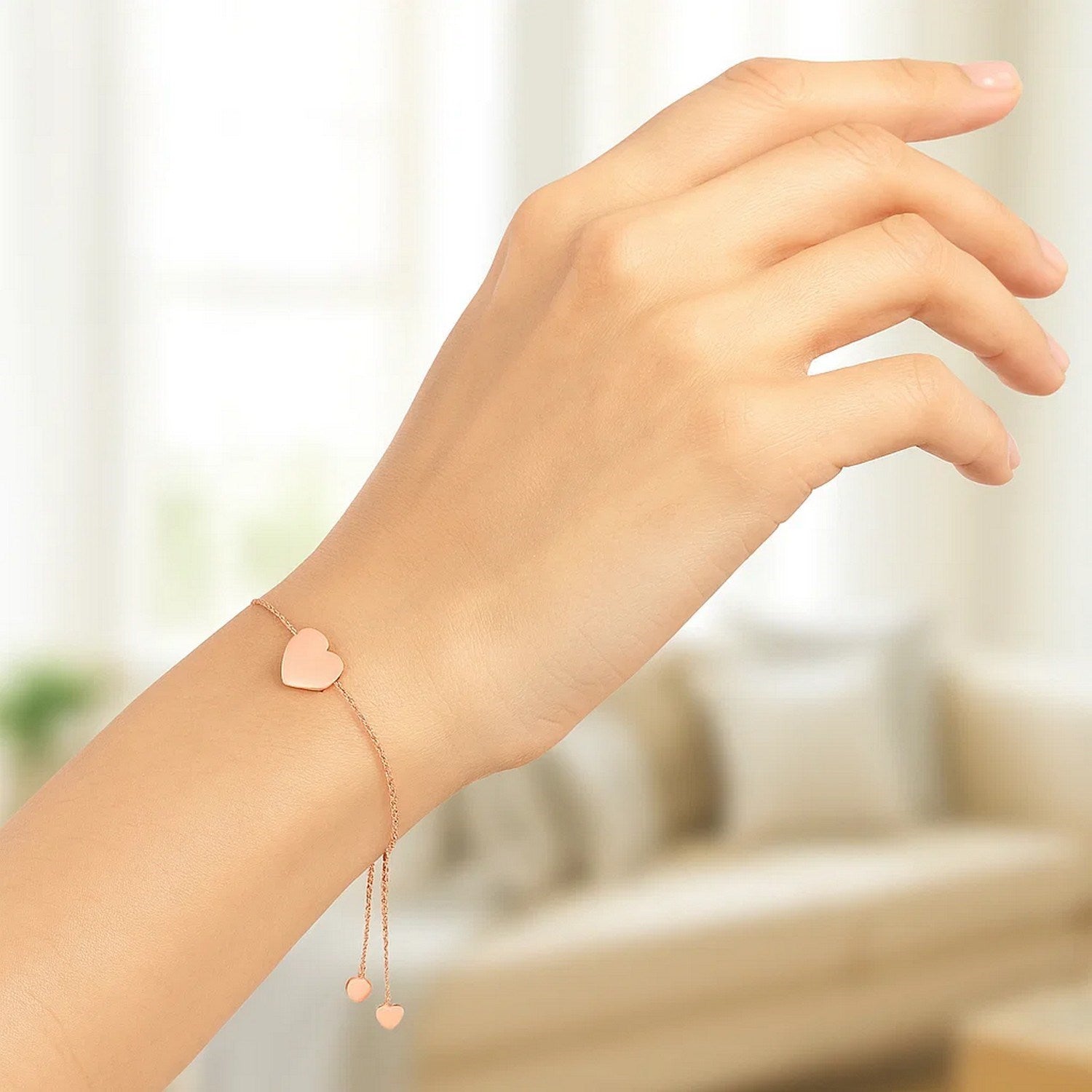A rose gold adjustable bracelet with a polished heart and two small dangling hearts.