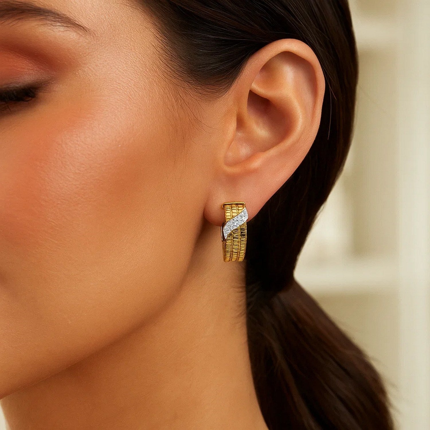 14K yellow gold triple row diamond omega hoop earrings on a woman's ear.