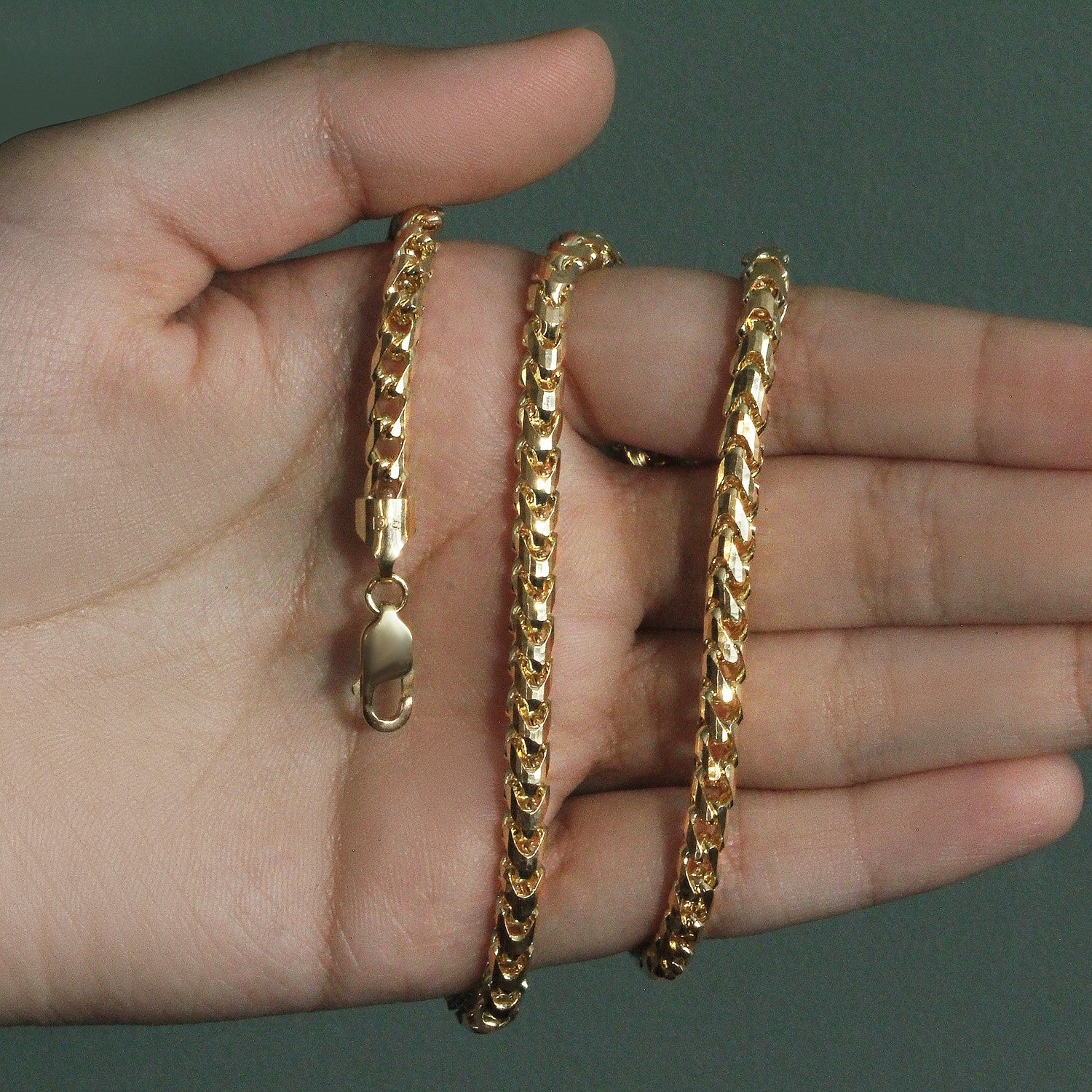 A 14k yellow gold diamond-cut round Franco chain with a lobster clasp is held in a hand.
