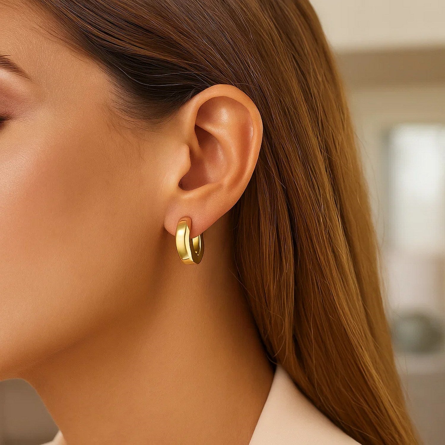 A woman wears a single 14K yellow gold thick post hoop earring.