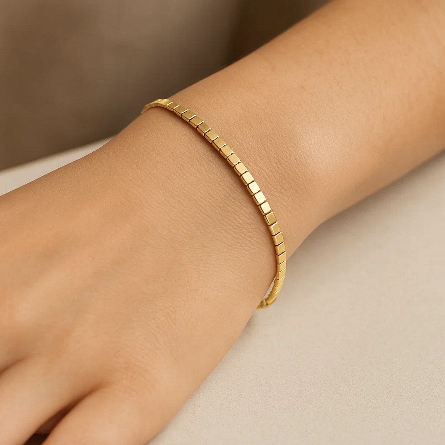 A 14K yellow gold mini cube bracelet is worn on a person's wrist.