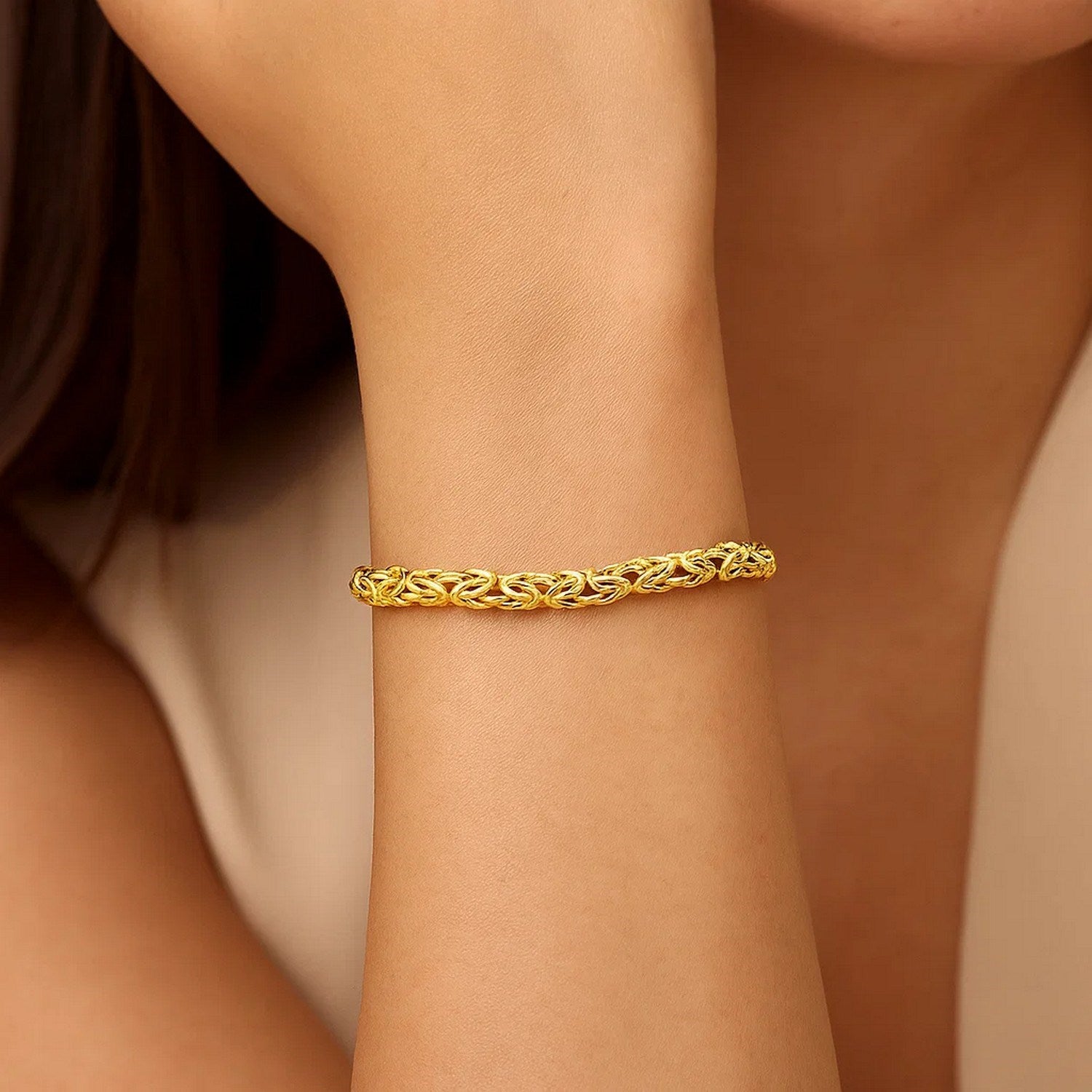 14k yellow gold Byzantine link shiny bracelet on a model's wrist.