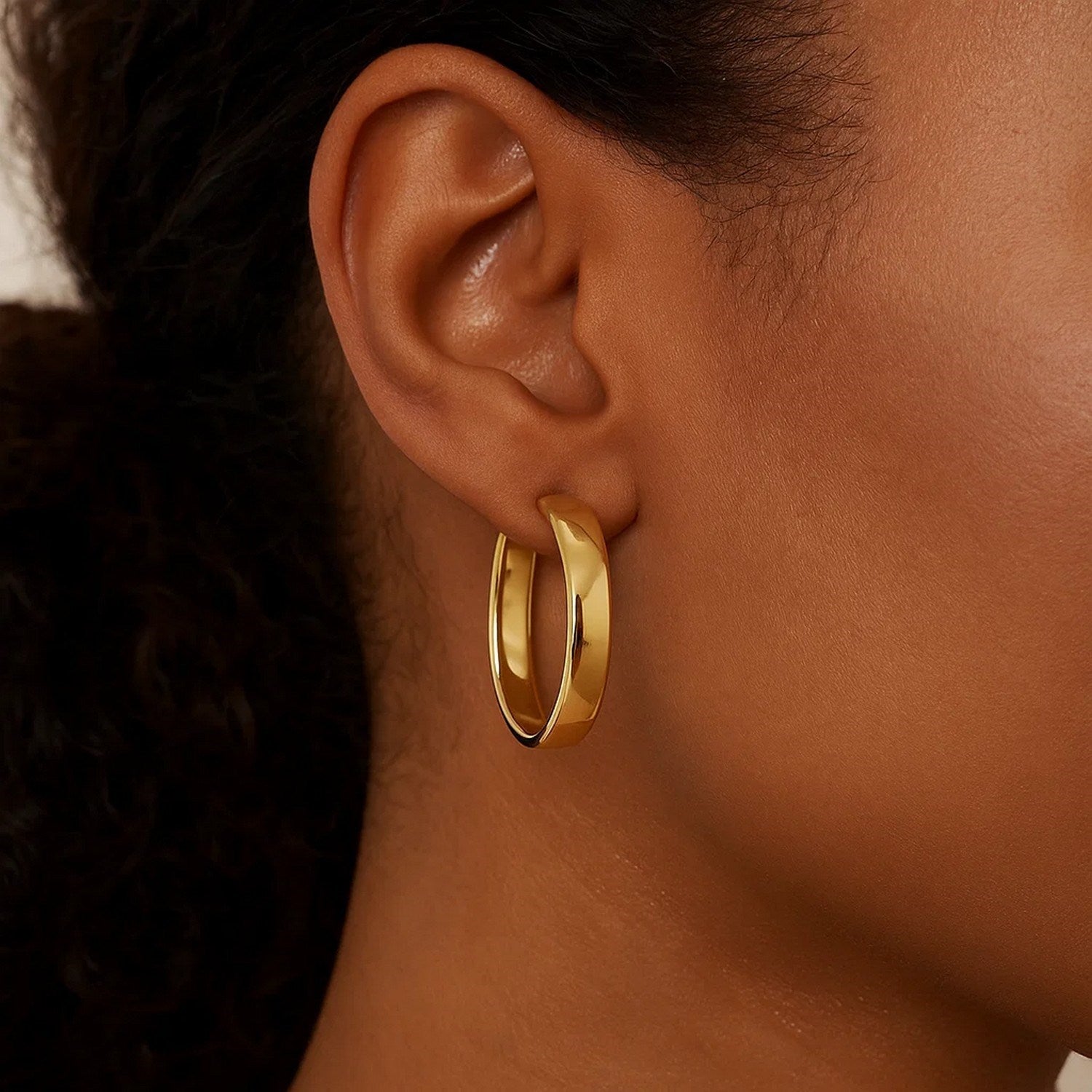 A woman wears a single 14k yellow gold wedding band hoop earring.