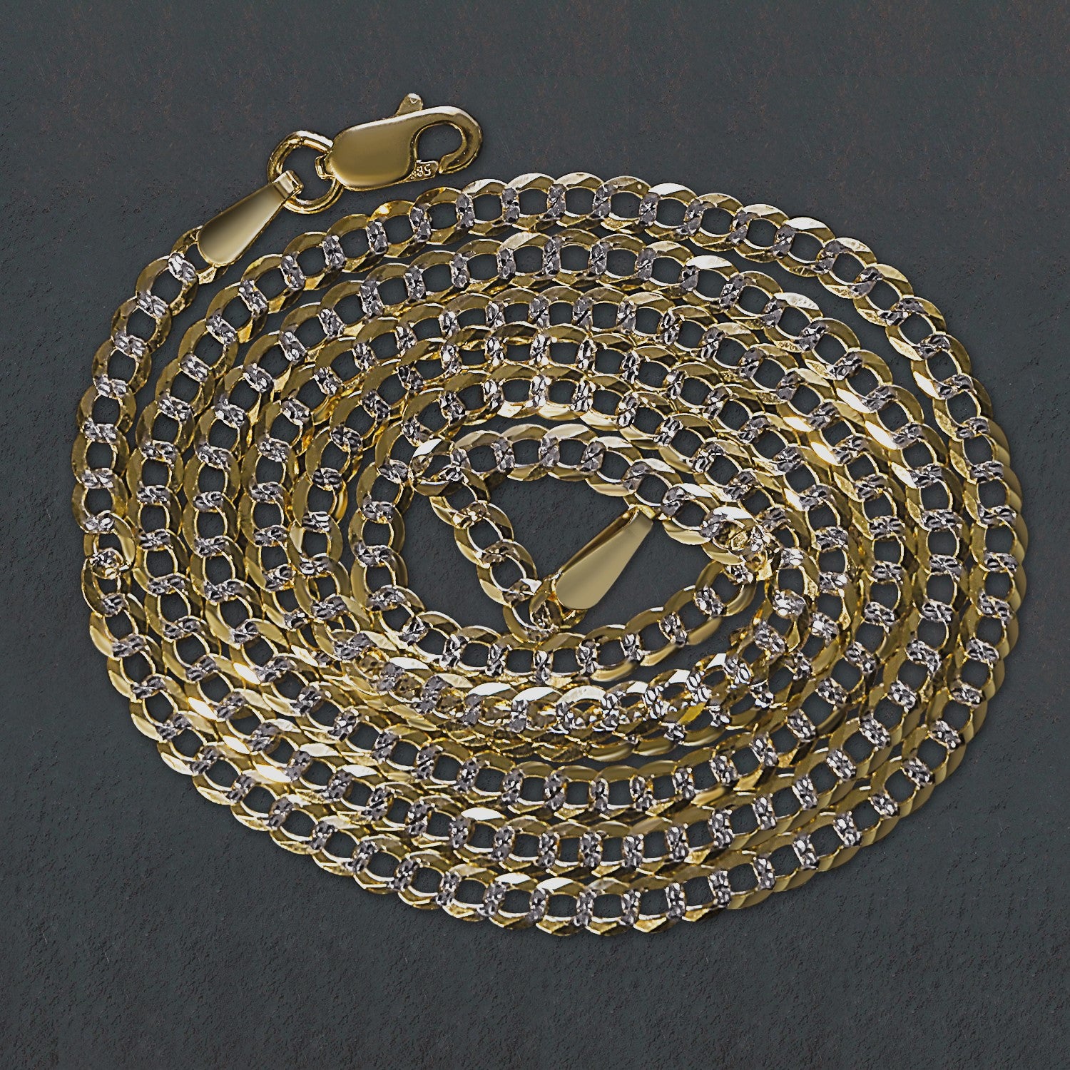 14k two-tone gold pave curb chain with a lobster clasp, coiled on a dark surface.