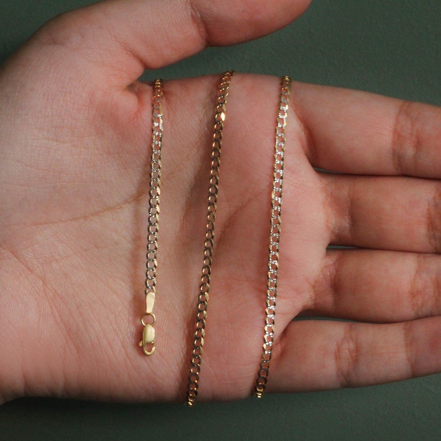 14k two-tone gold pave curb chain with a lobster clasp, held in an open hand.
