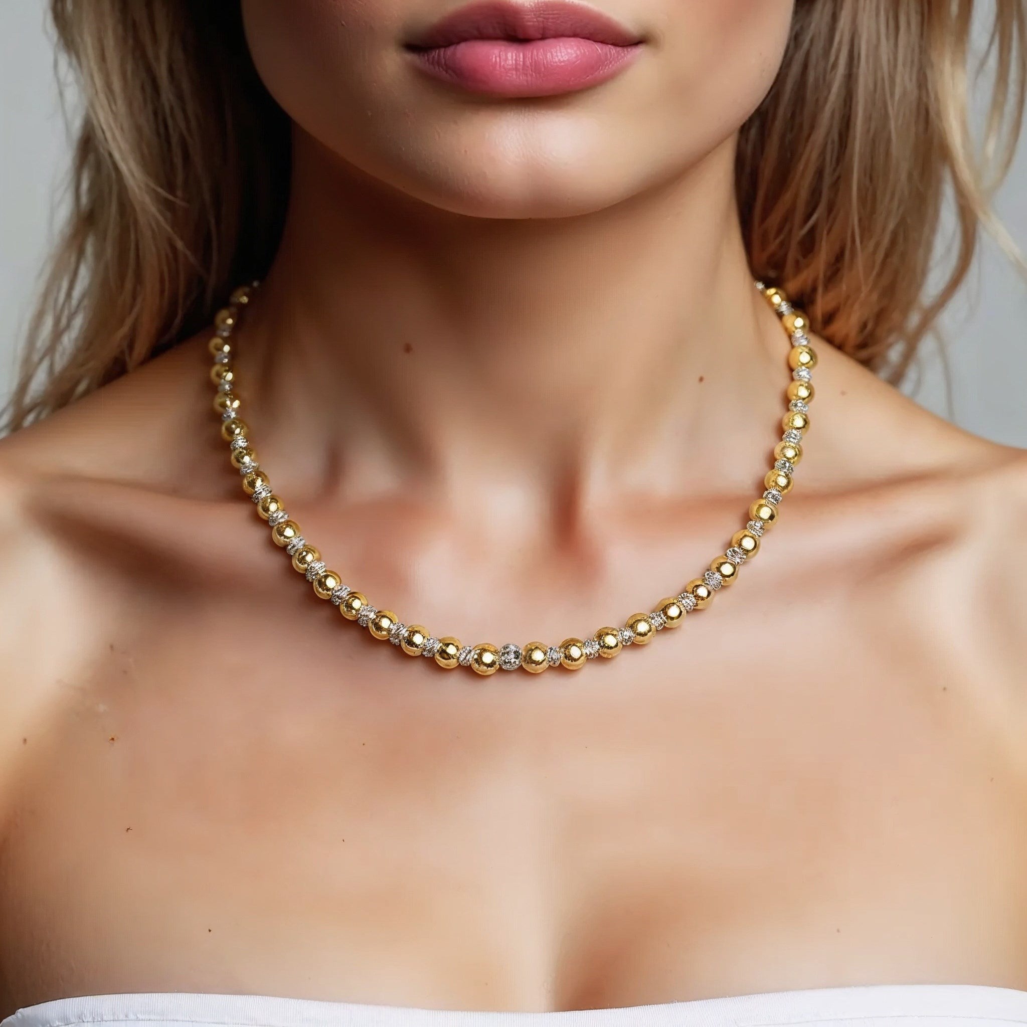 A two-tone beaded chain necklace in 14K gold on a person's neck.