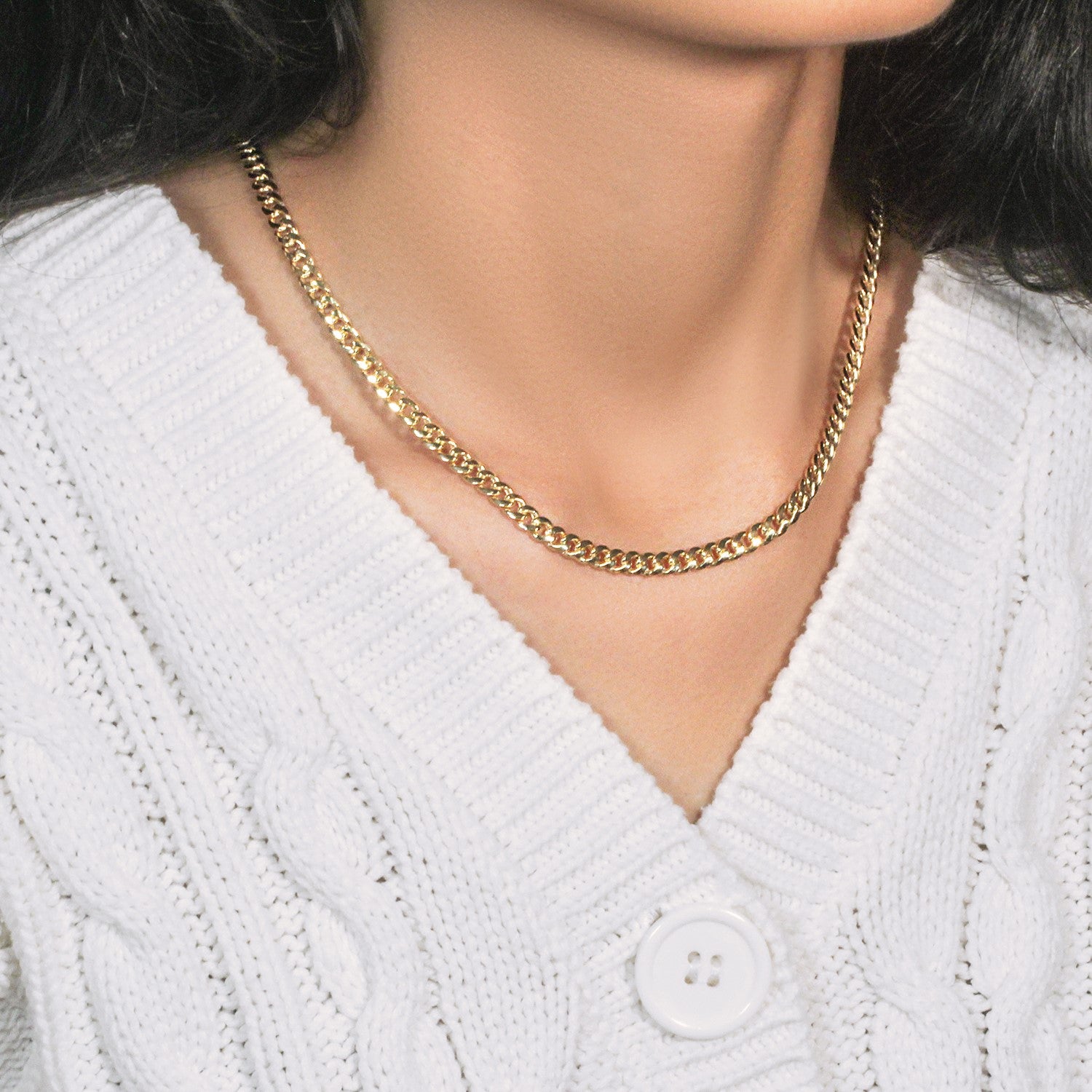 A woman wears a 10k yellow gold Miami Cuban chain over a white cable-knit sweater.