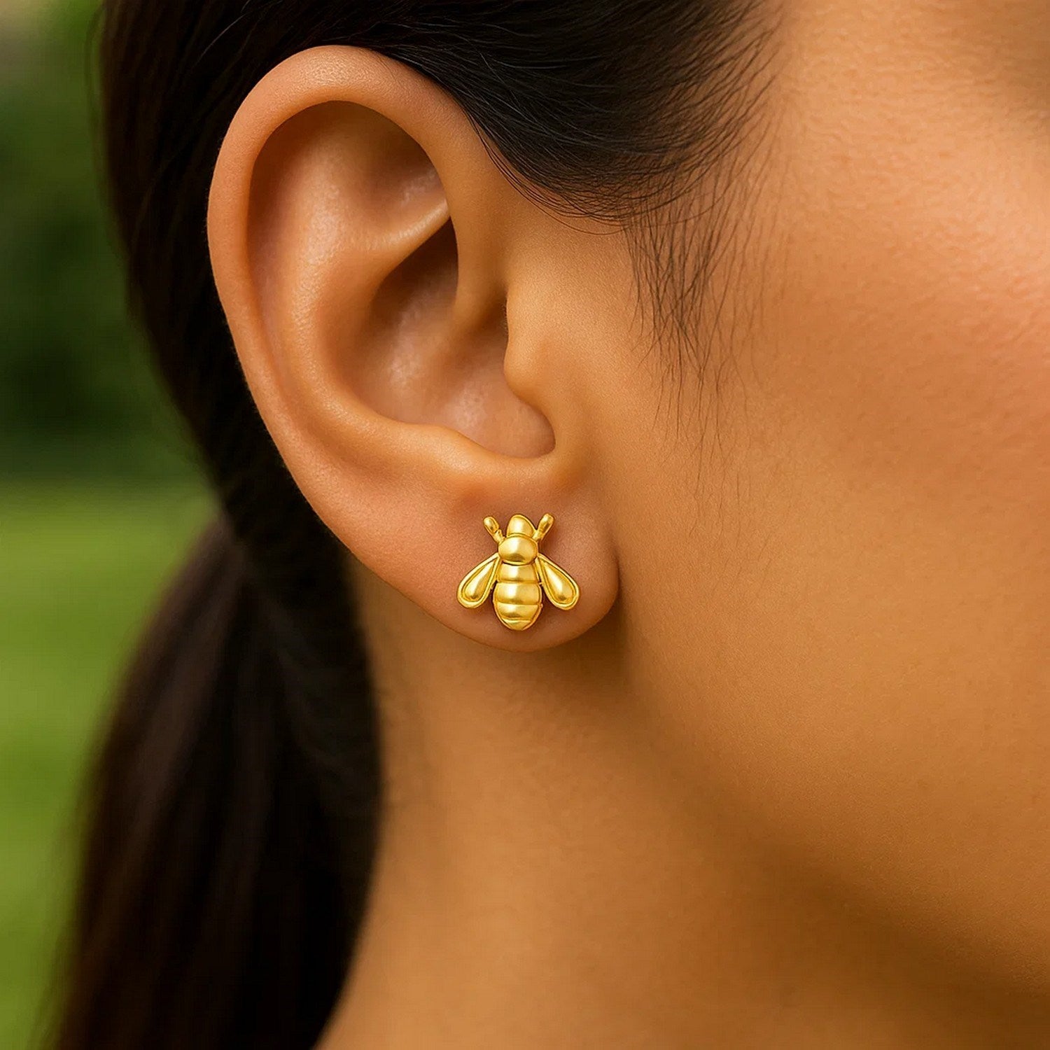 14k yellow gold bee stud earring on a person's ear.