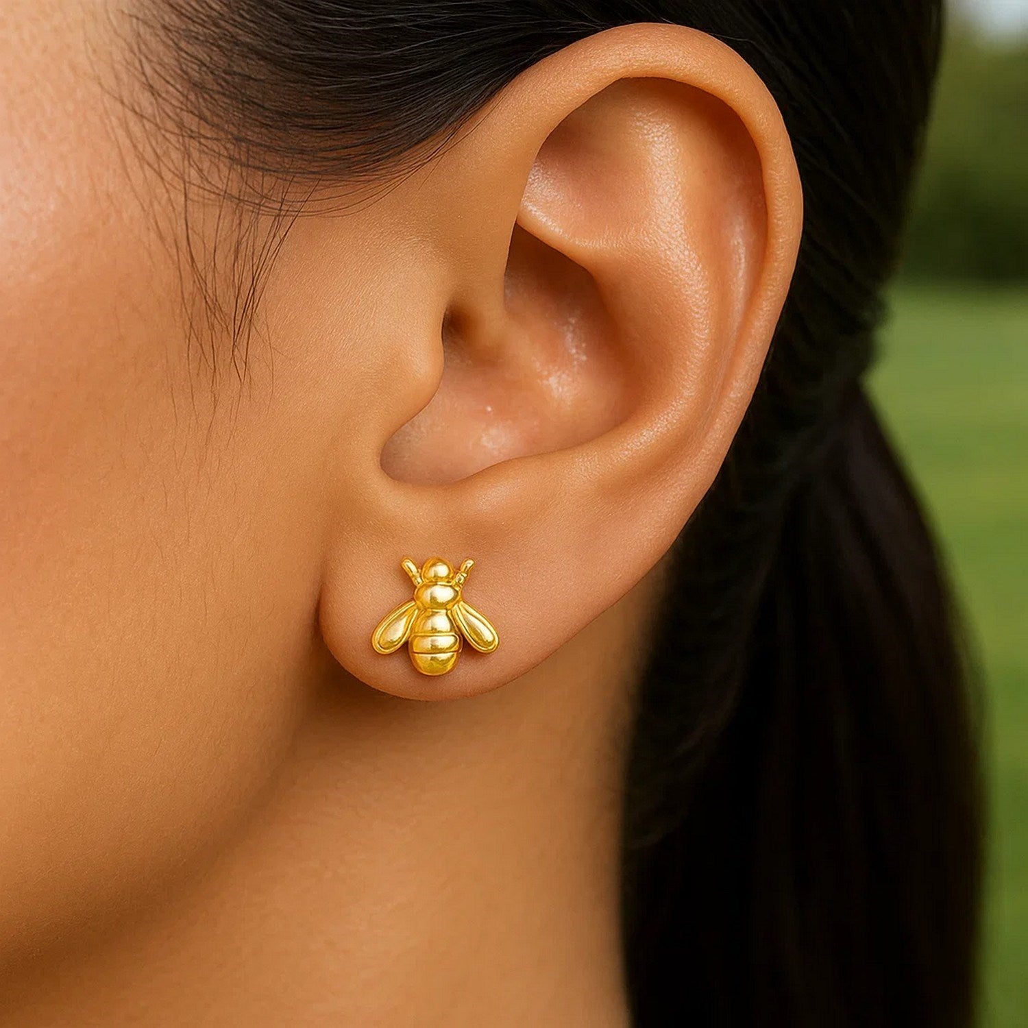 A single 14k yellow gold bee stud earring is worn on an ear.