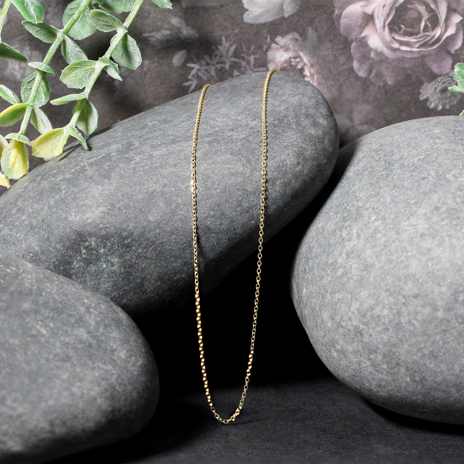 10k yellow gold diamond cut cable link chain draped over smooth gray stones.