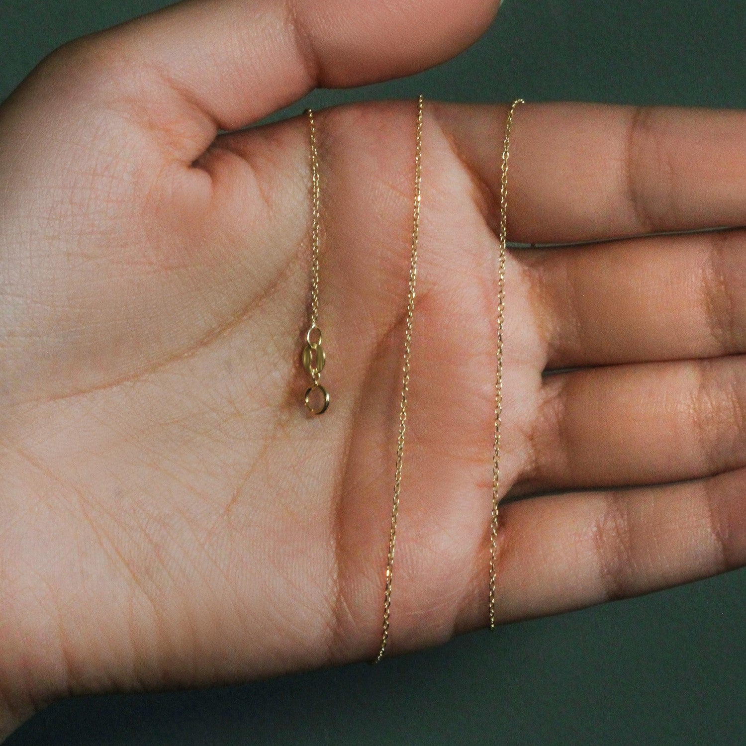 A 10k yellow gold diamond-cut cable link chain with a lobster clasp rests on a hand.