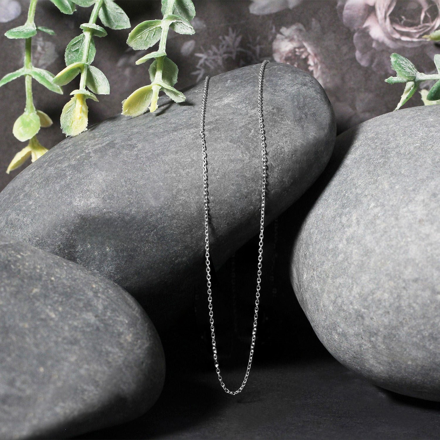 18k white gold diamond cut cable link chain draped over smooth gray stones.