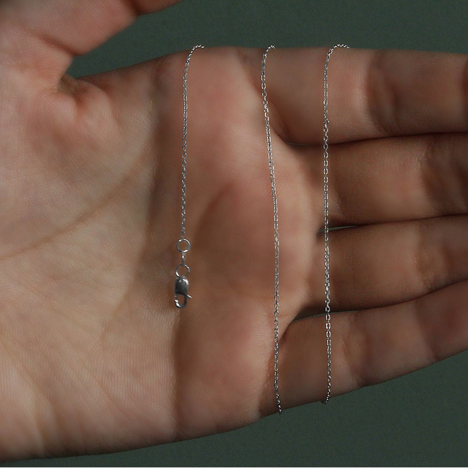 18k white gold diamond cut cable link chain with a lobster clasp, held in a hand.