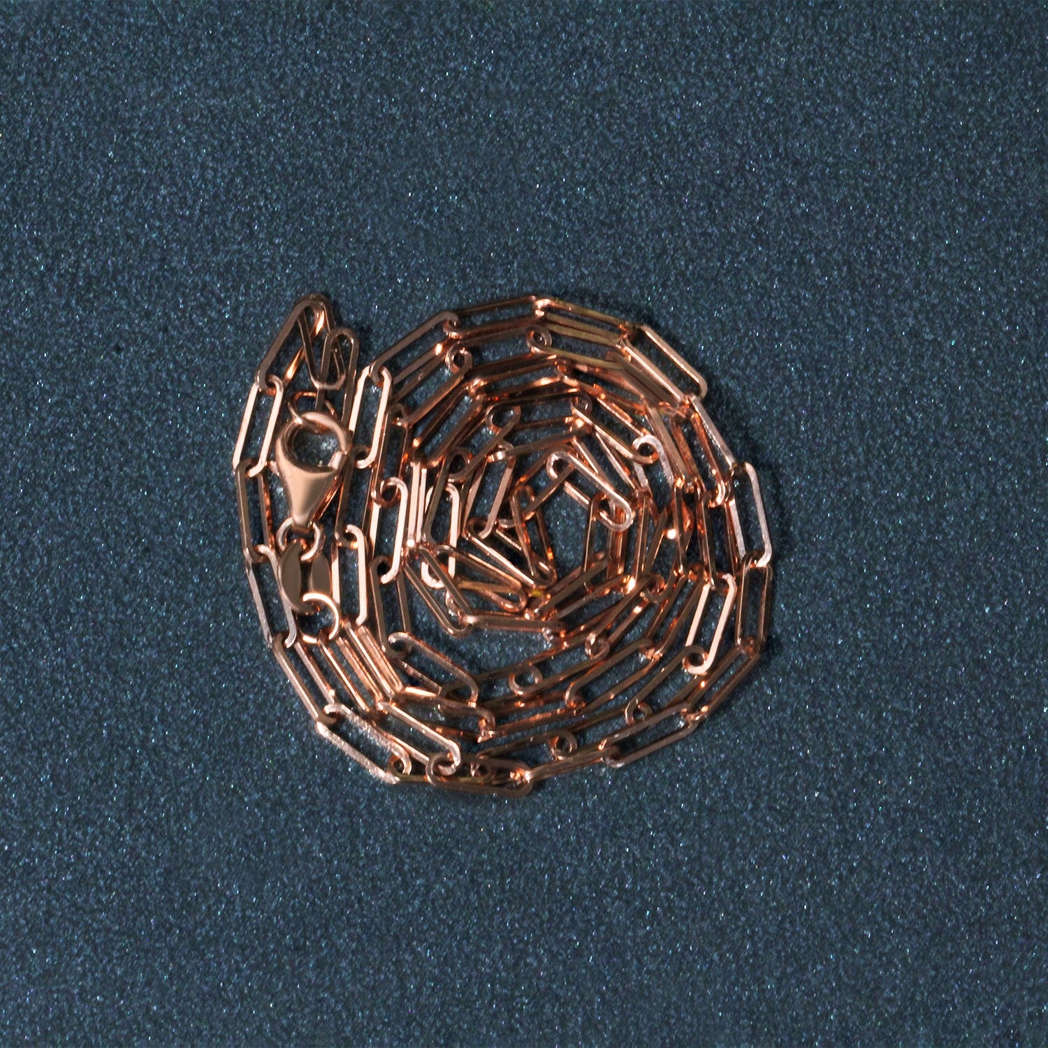 14K rose gold delicate paperclip chain with a lobster clasp, coiled on a dark background.