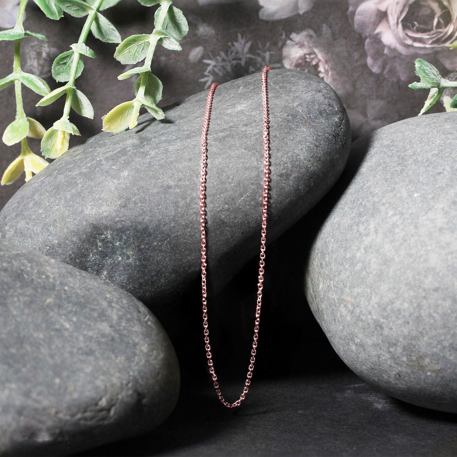 18k rose gold diamond cut cable link chain draped over dark grey stones.