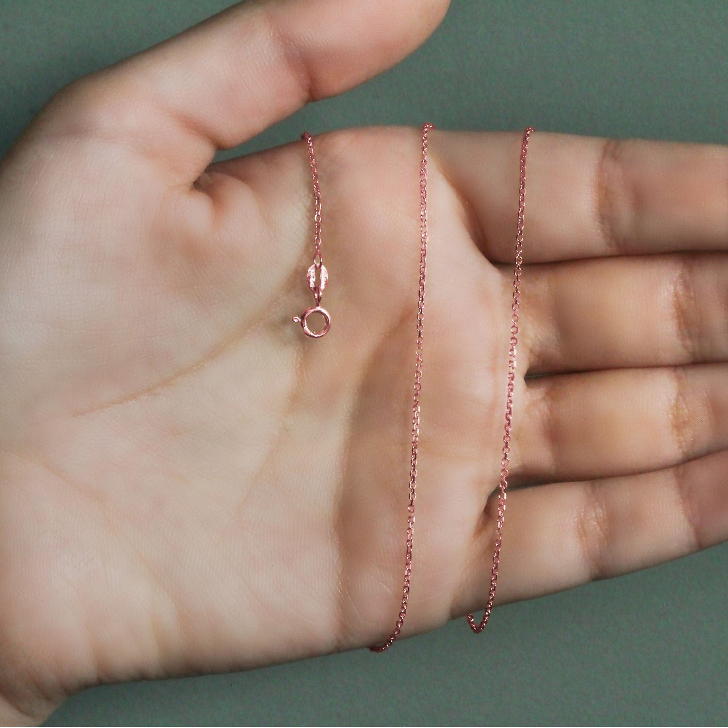 18k rose gold diamond cut cable link chain with a spring ring clasp on a hand.