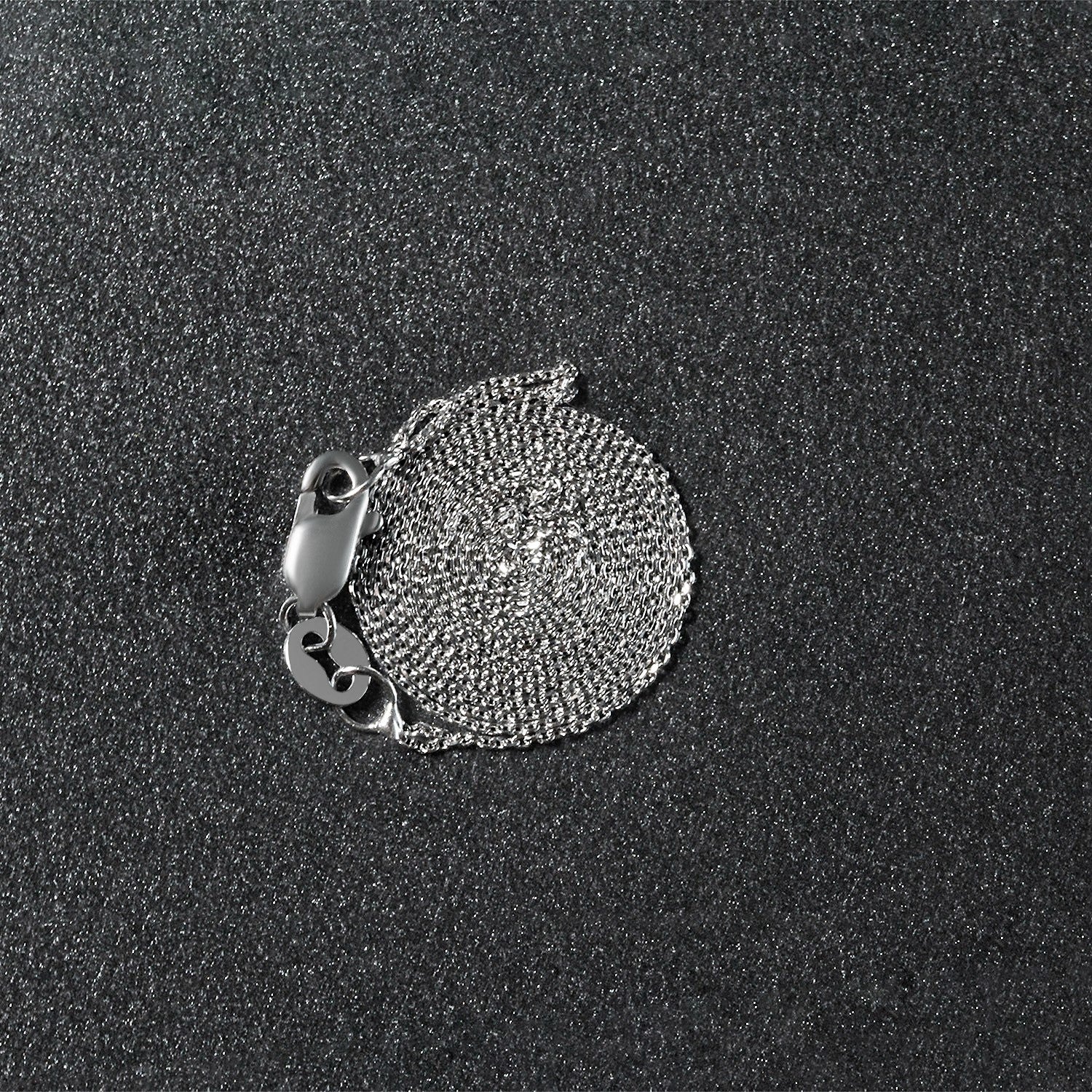 A coiled 14k white gold cable link chain with a lobster clasp on a dark, textured surface.