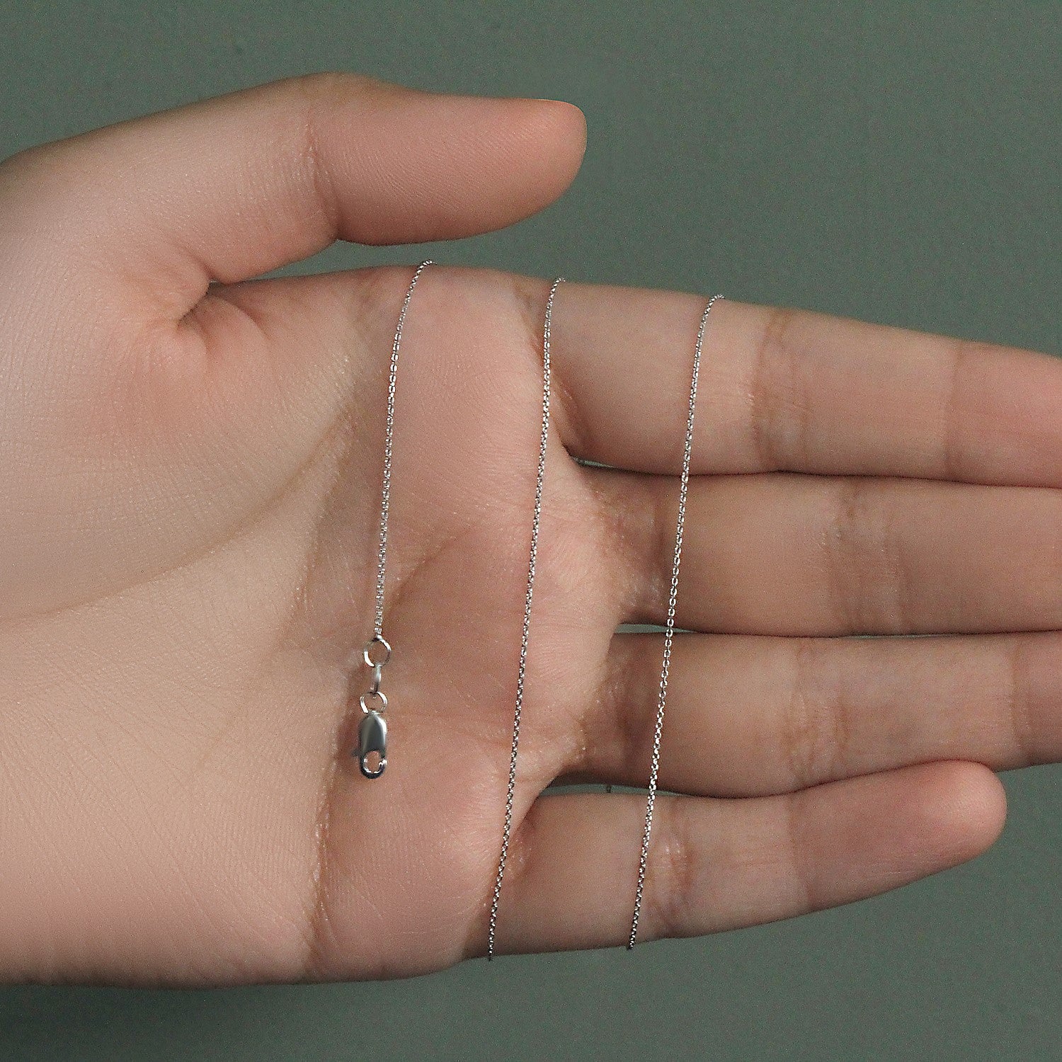 A 14k white gold cable link chain with a lobster clasp rests on a hand.