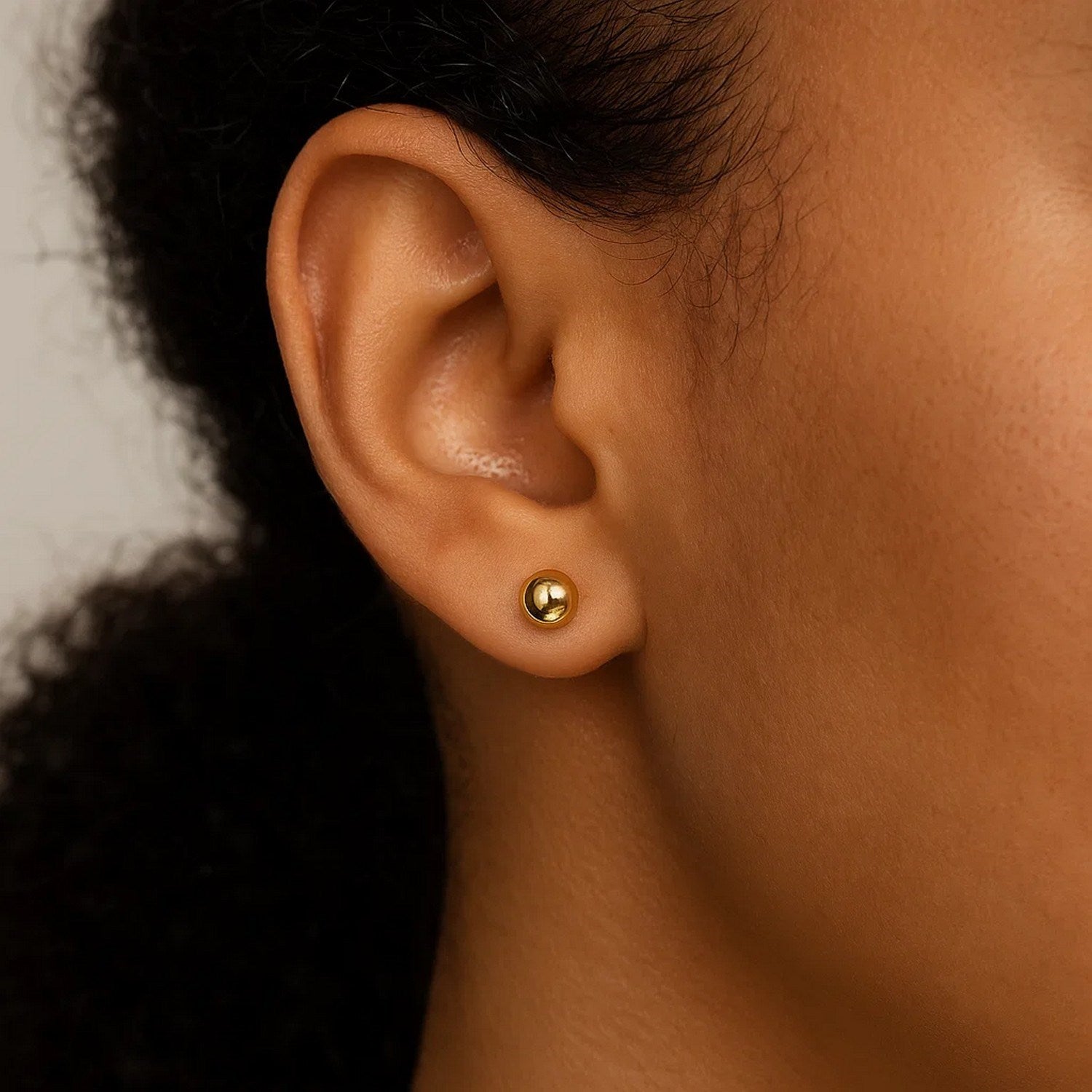 A single 10k yellow gold round stud earring is worn on an ear.