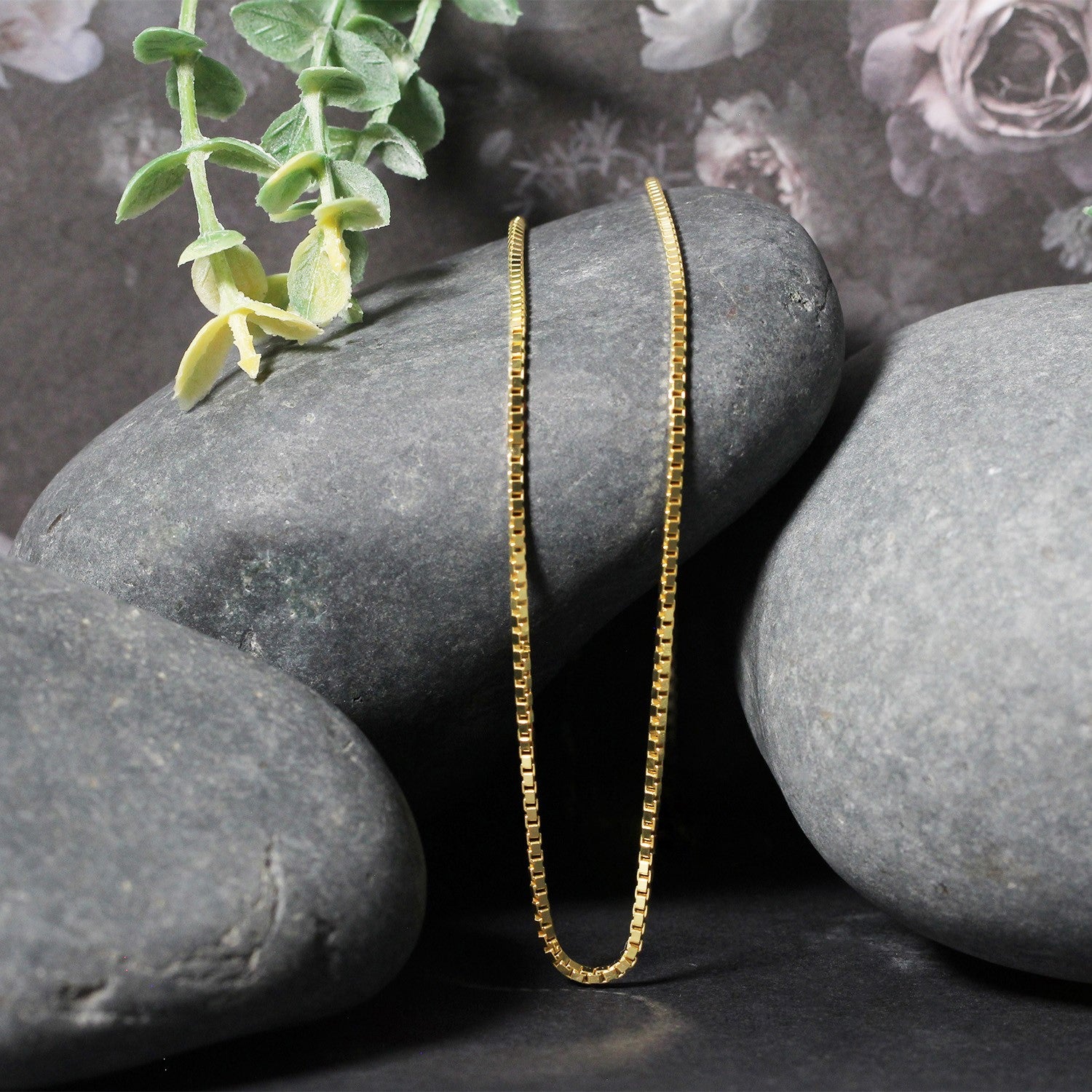 A 10k yellow gold classic box chain rests on dark grey stones.