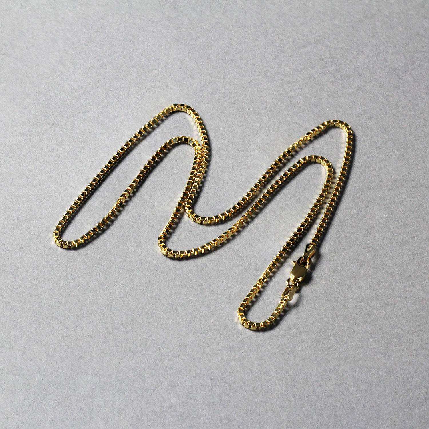 A 10k yellow gold classic box chain with a lobster clasp lies on a gray surface.