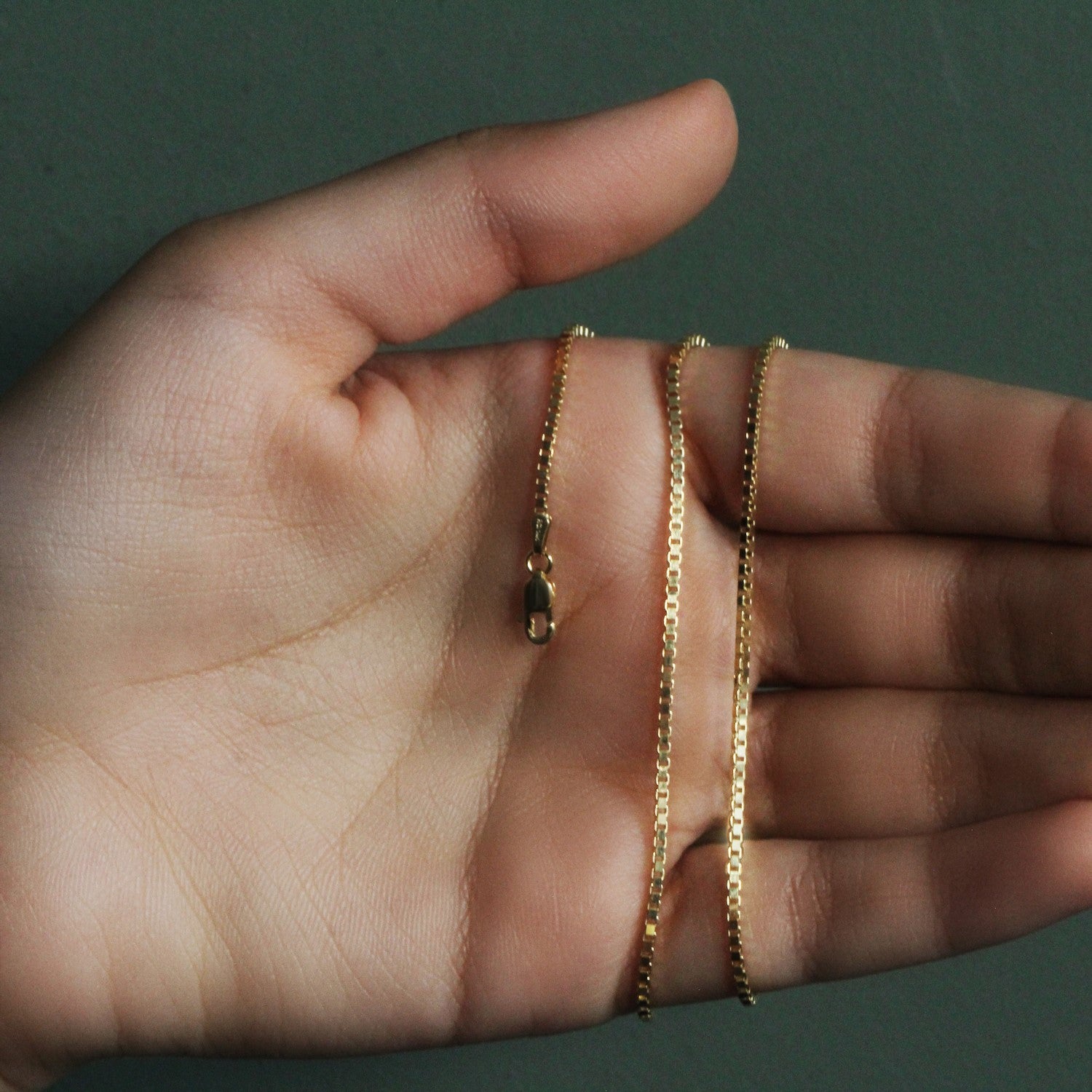 A 10k yellow gold classic box chain with a lobster clasp is held in a hand.