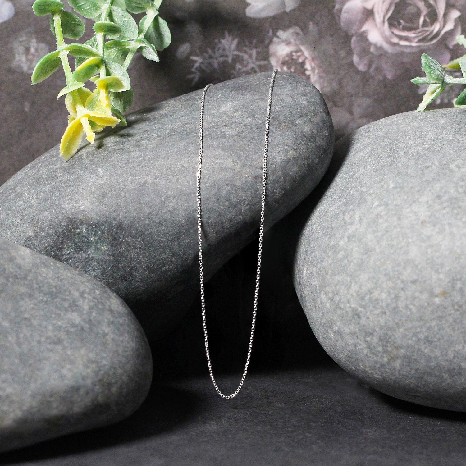 A delicate 14k white gold diamond-cut cable link chain draped over smooth grey stones.